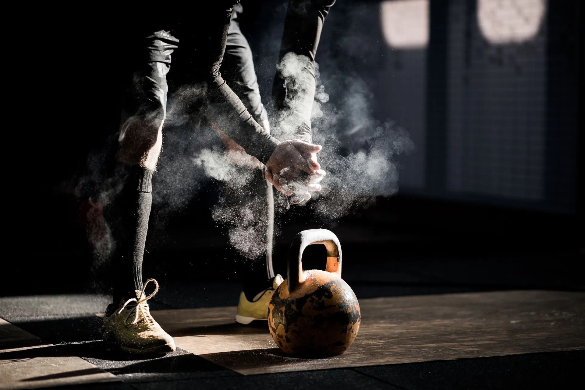 Rustic kettlebell and chalk-dusted weight plates on a dark gym floor, lit by a spotlight