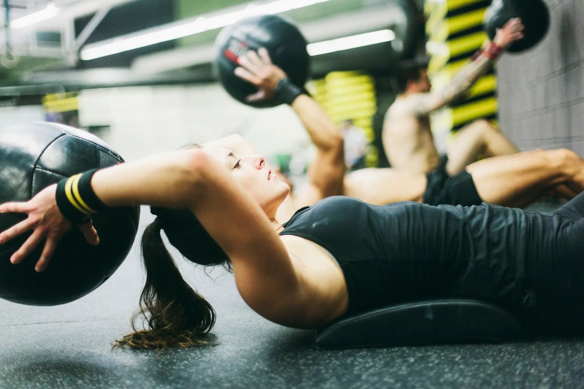 People doing dumbbell exercises on gym mats, one in the foreground holding a weight overhead