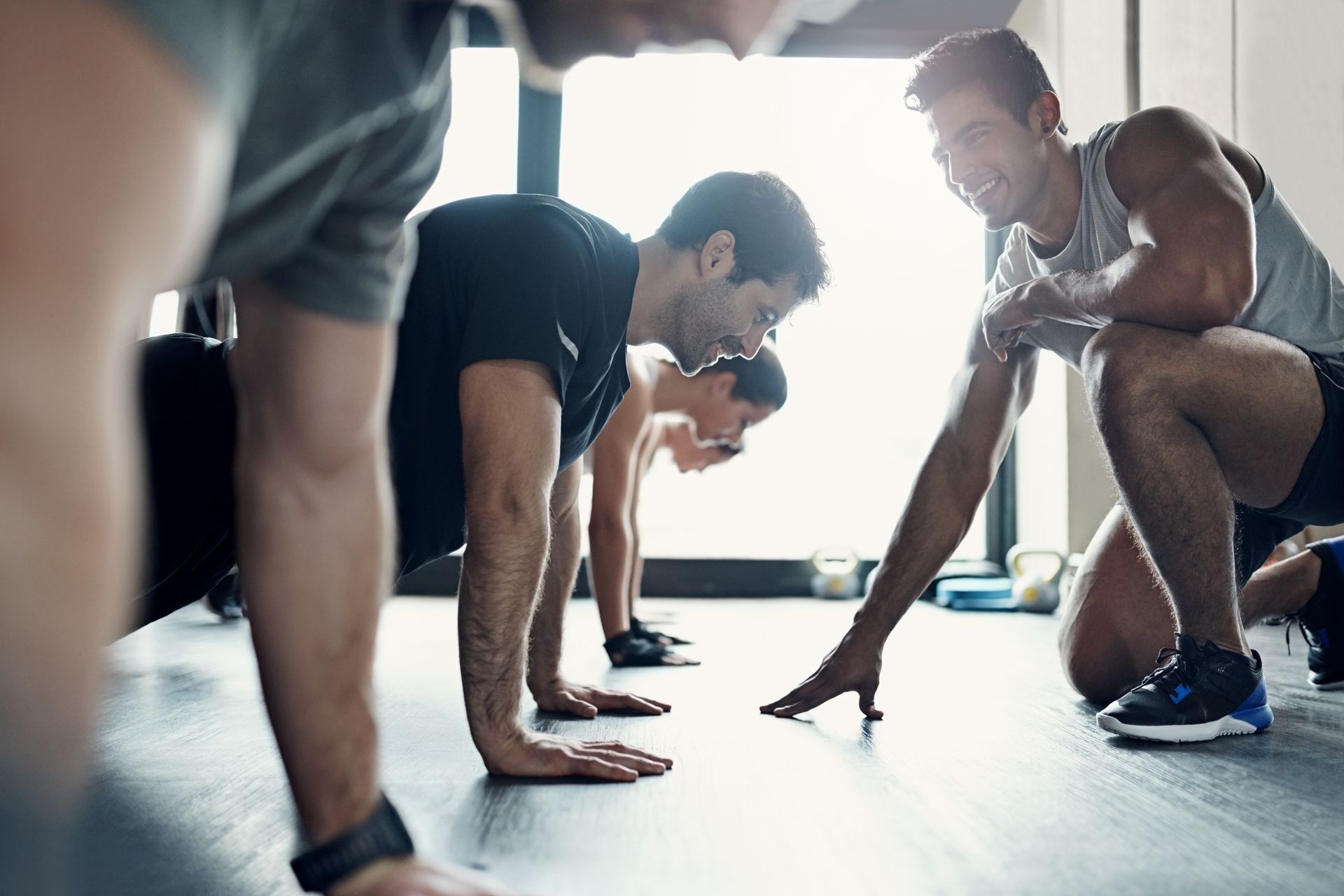 People in a gym doing plank exercises on a bright floor, focused on a workout.