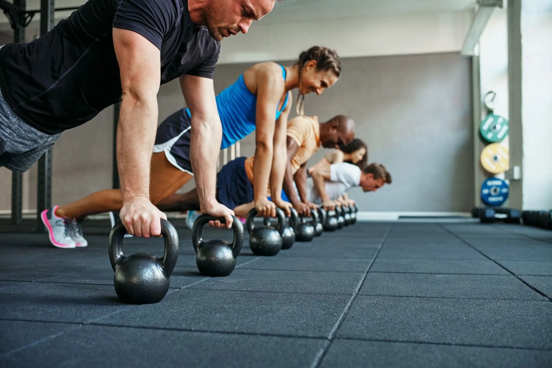 People doing kettlebell rows in a gym, lined up on black rubber flooring.
