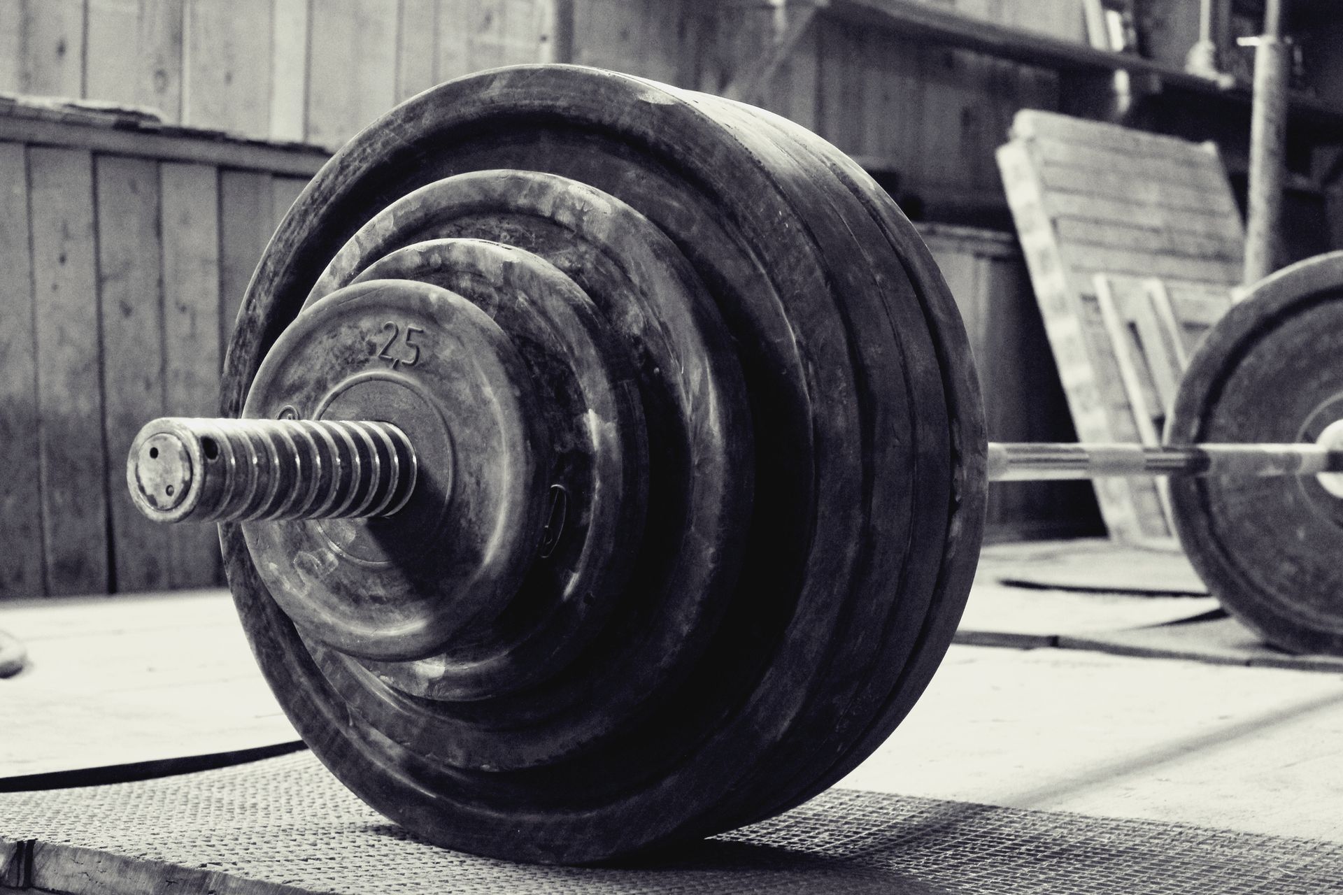 Heavy barbell with weight plates resting on a gym floor in front of a wooden fence