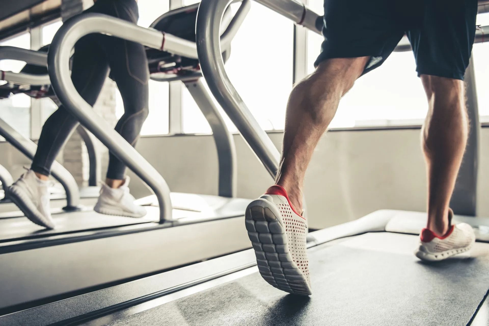 People walking on treadmills in a gym, shown from the side at leg level