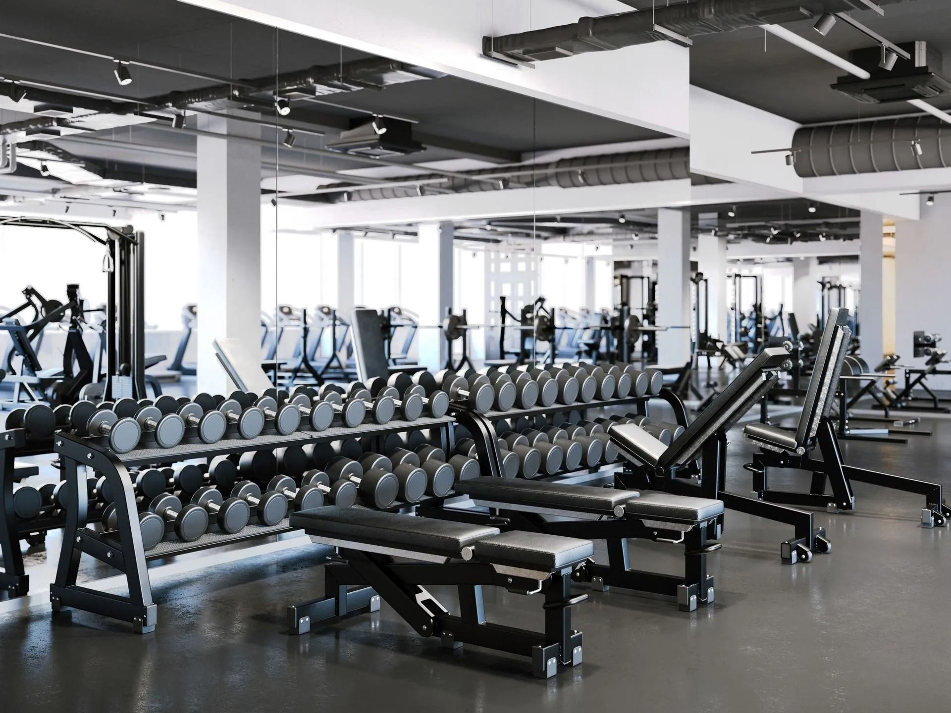 Modern gym with rows of dumbbells, benches, and workout machines in a bright mirrored room