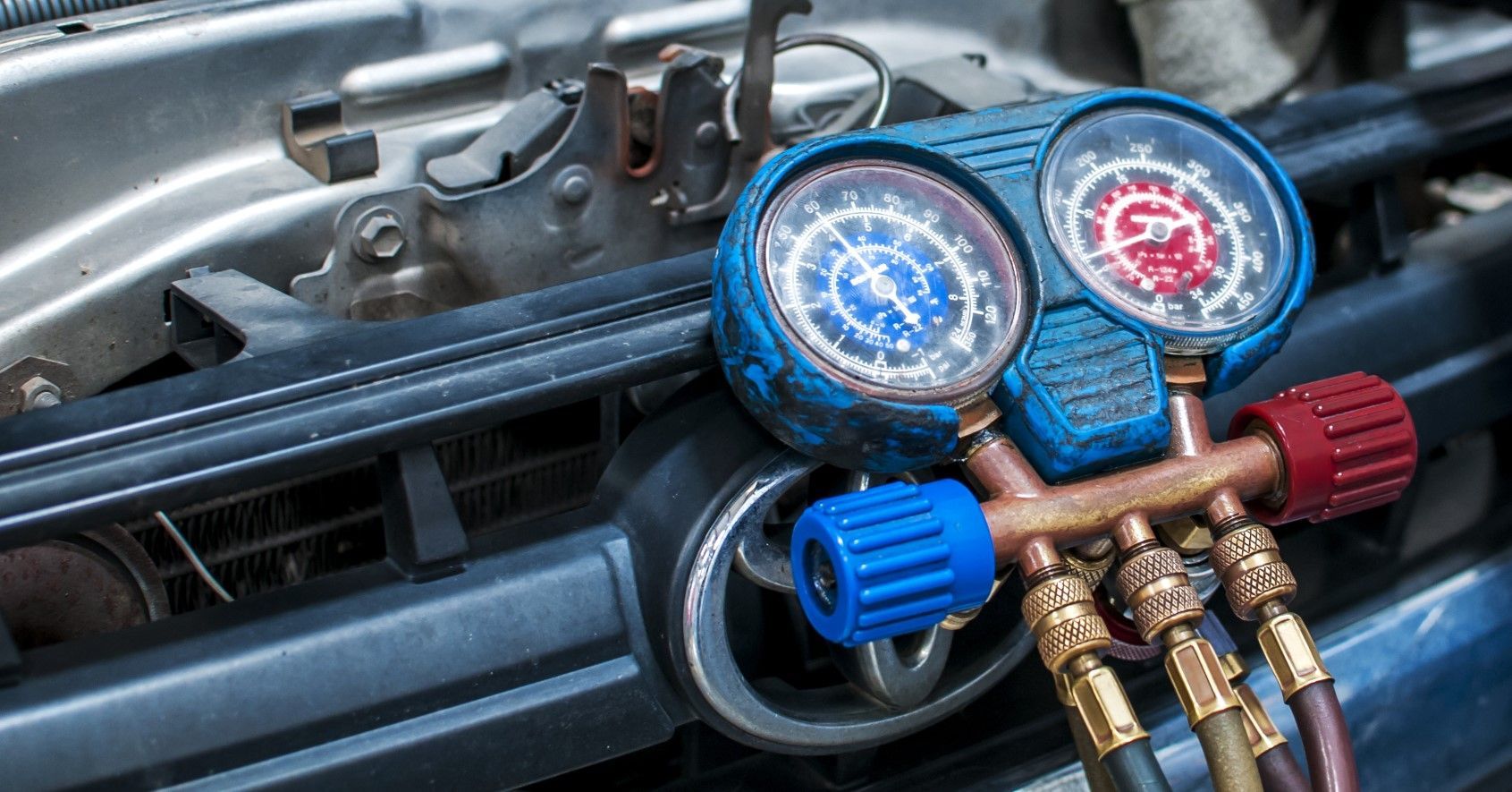 Close-up of car engine with an AC gauge set attached, measuring pressure; blue and red gauges.