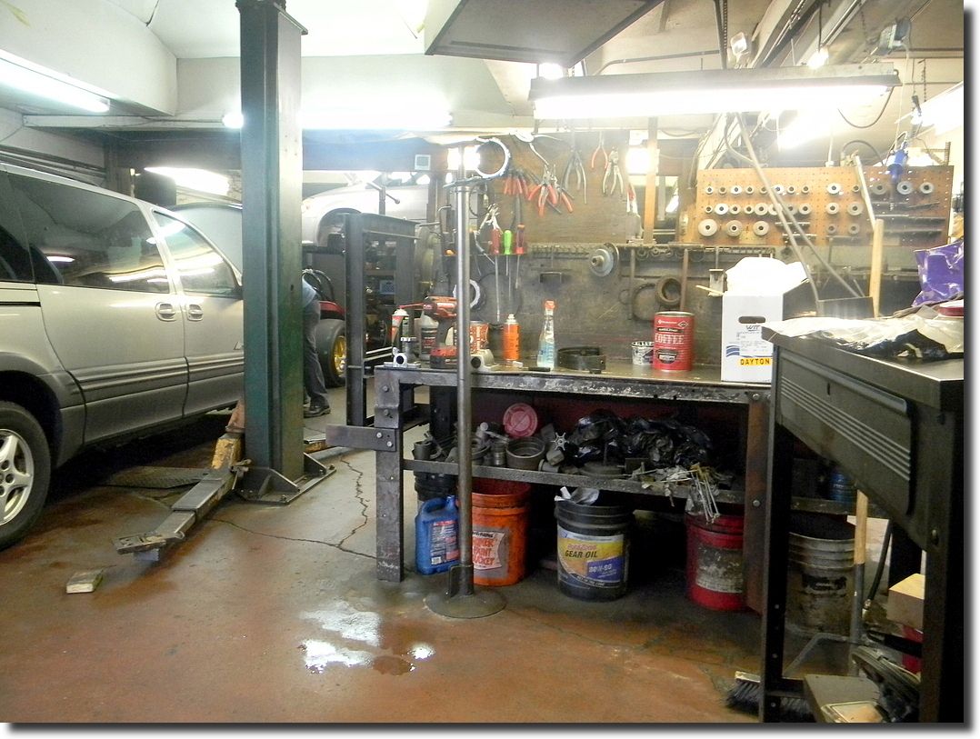 Auto repair shop with a vehicle on a lift, cluttered workspace, tools, and a technician visible.