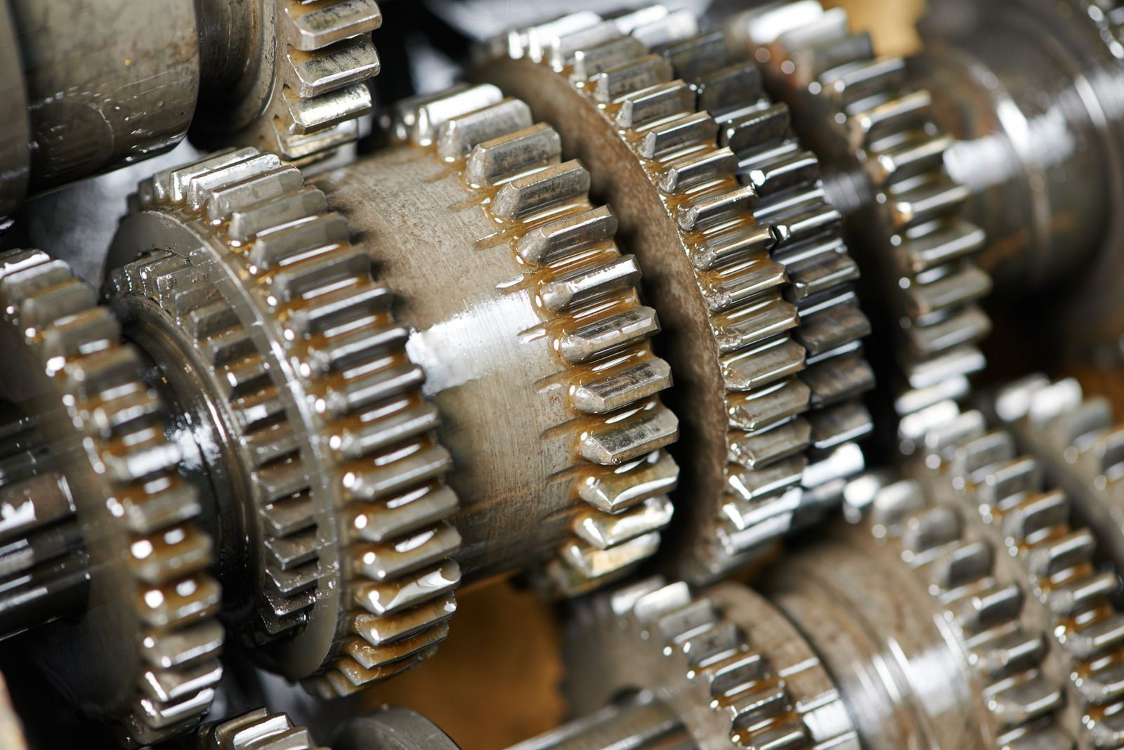Close-up of metal gears meshed together, covered in oil, inside a machine.