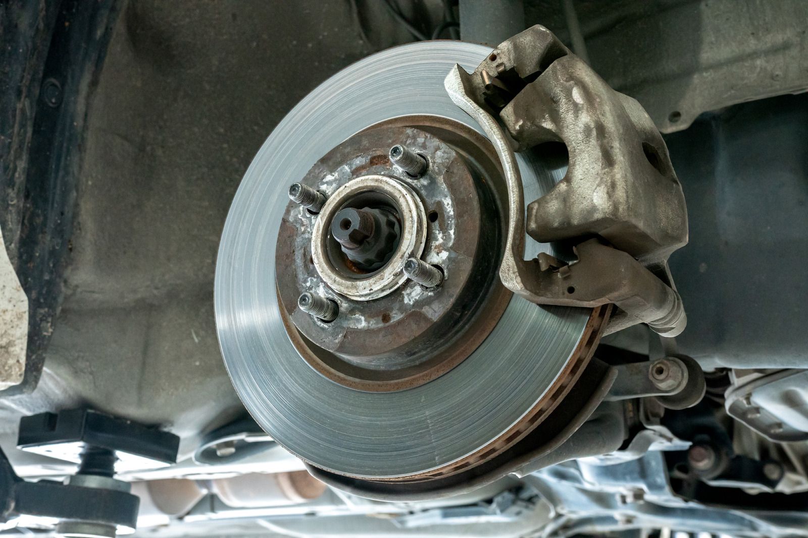 Car brake rotor and caliper assembly. Silver disc brake with a gray caliper attached, viewed from below.