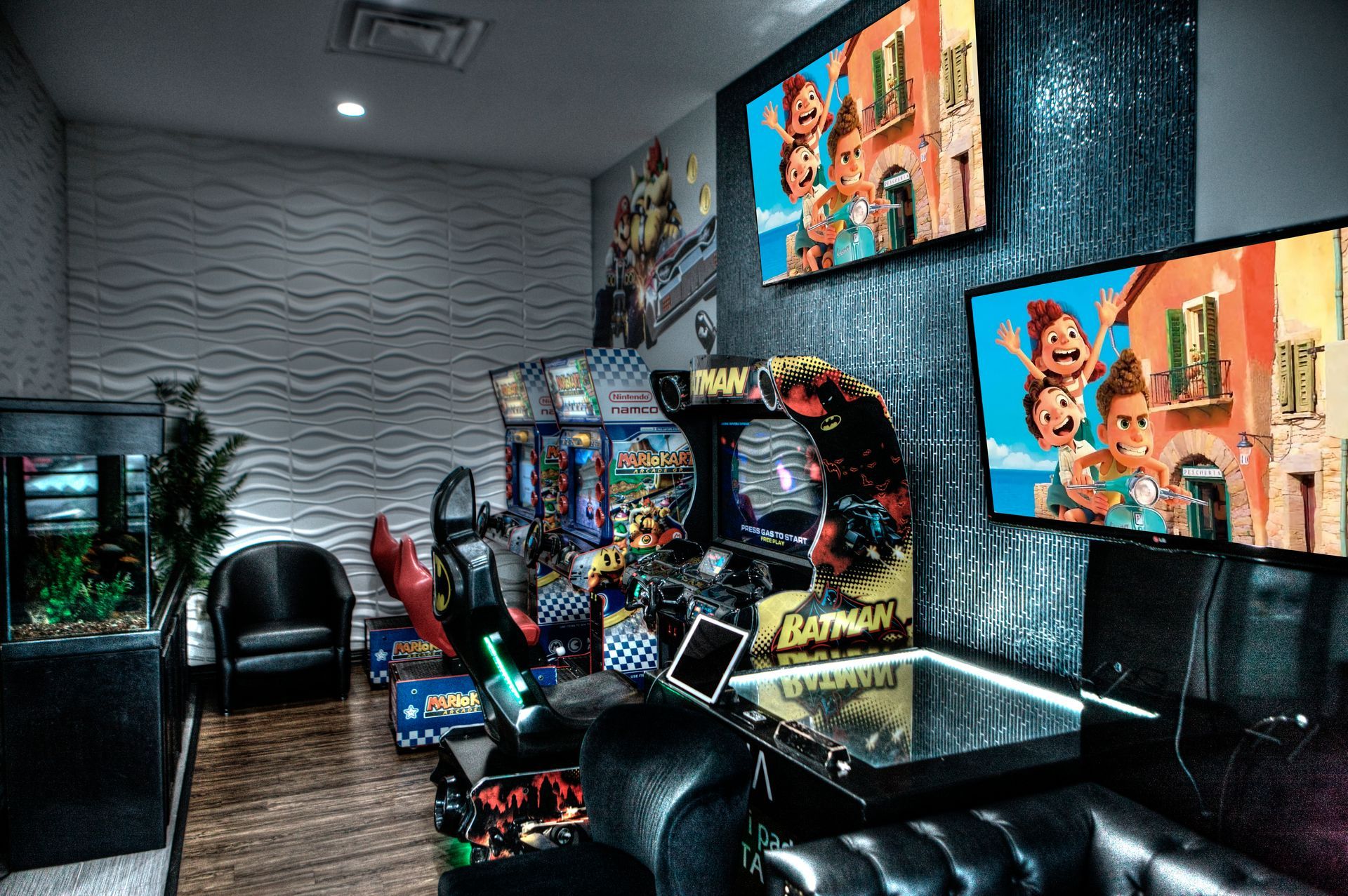 Luna-Dental-Dallas- Game room with arcade games, TVs showing animation, black leather seating, and aquarium.