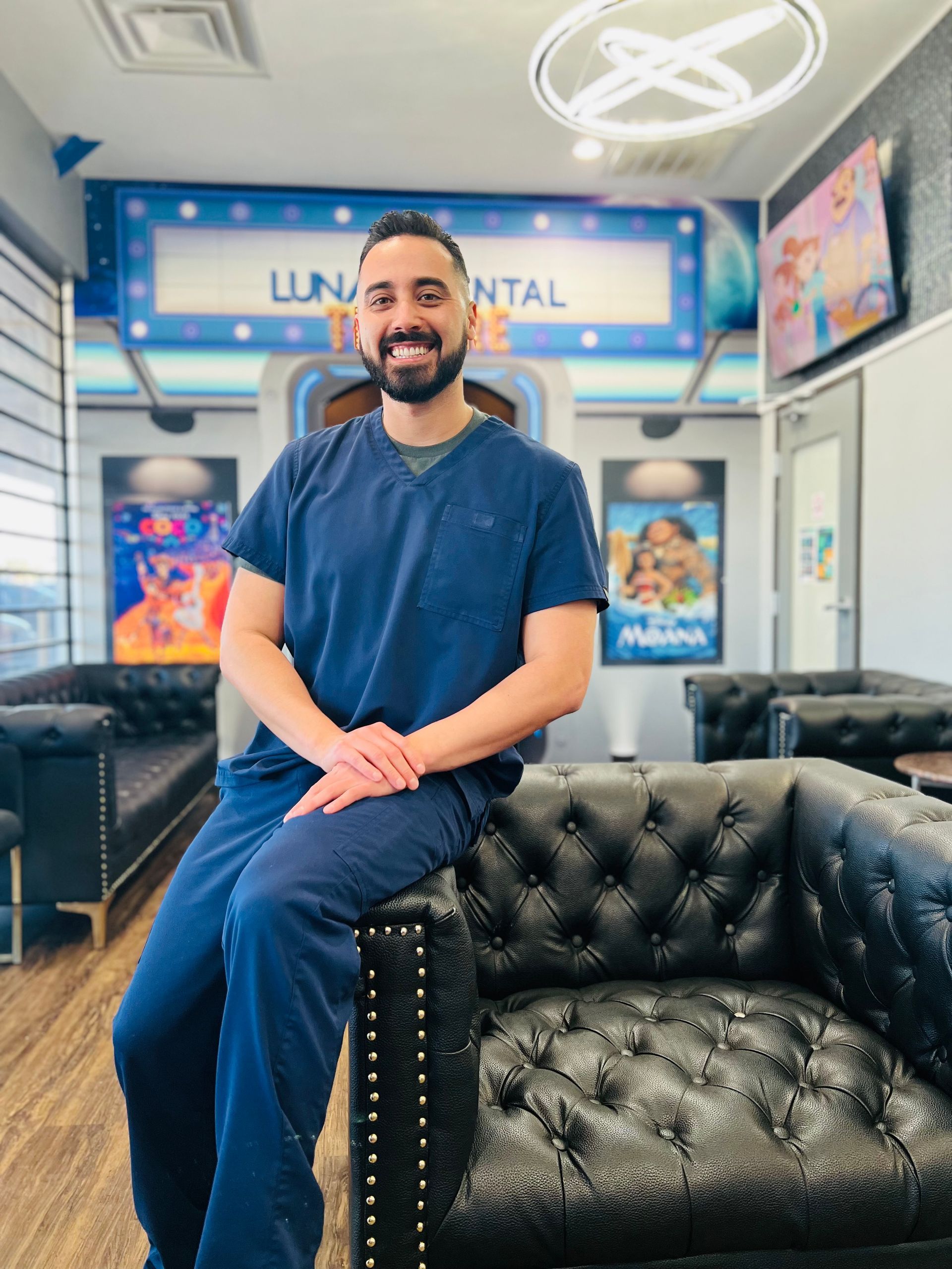 Luna-Dental-Dallas- Man in blue scrubs sitting on a black tufted couch in a dental office. The office is decorated with space-themed elements.