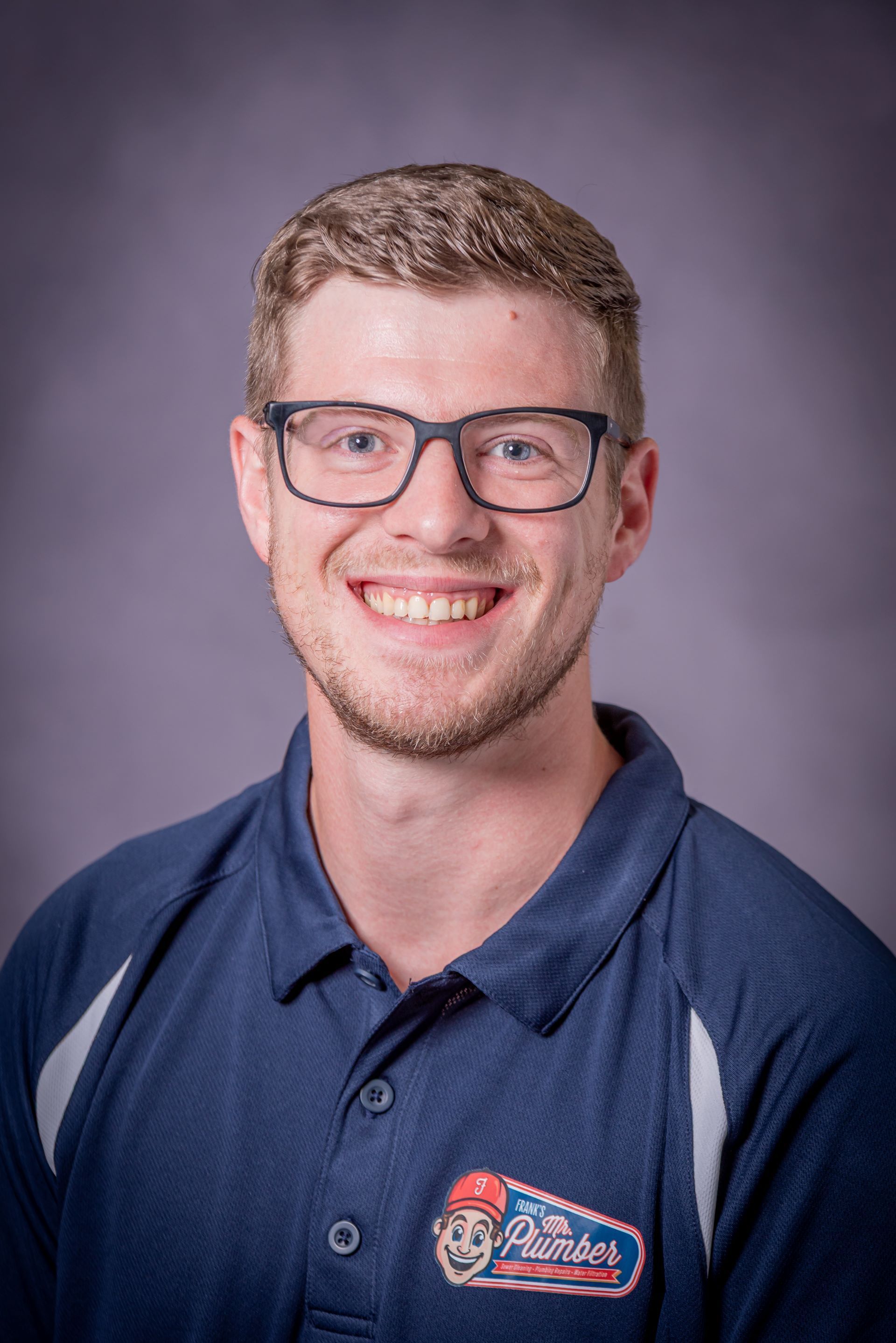 A young man wearing glasses and a blue polo shirt is smiling for the camera.