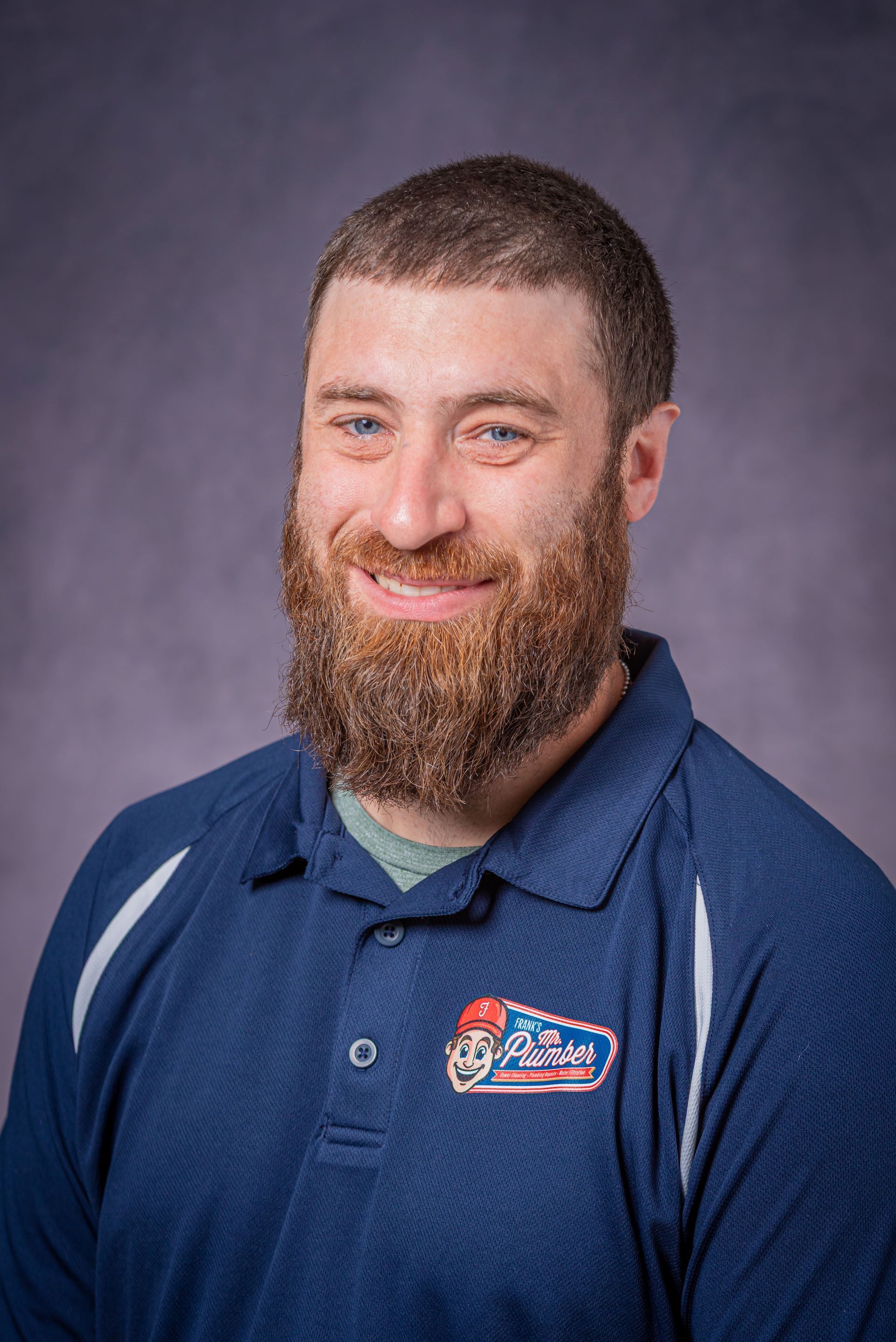 Man with beard wearing a blue polo shirt, smiling.