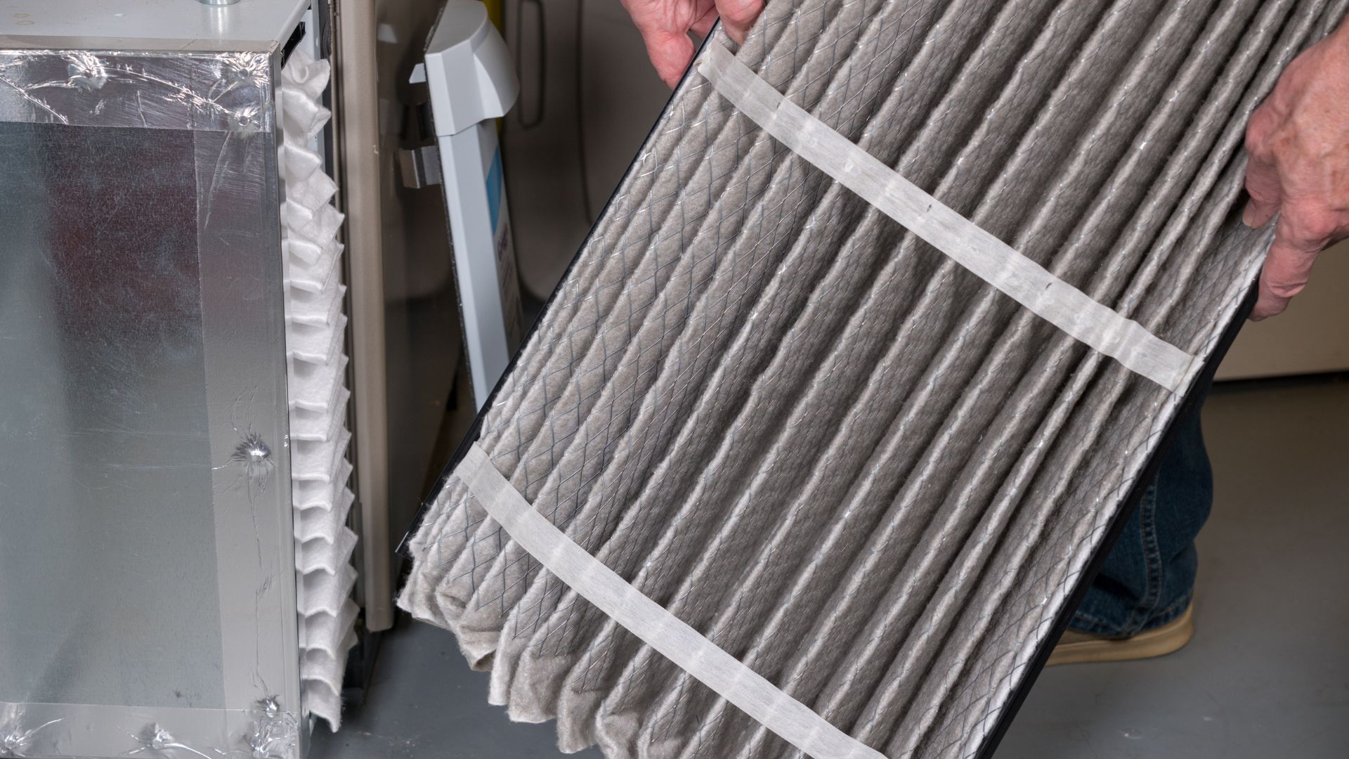 Person holding a dirty air filter next to a furnace.