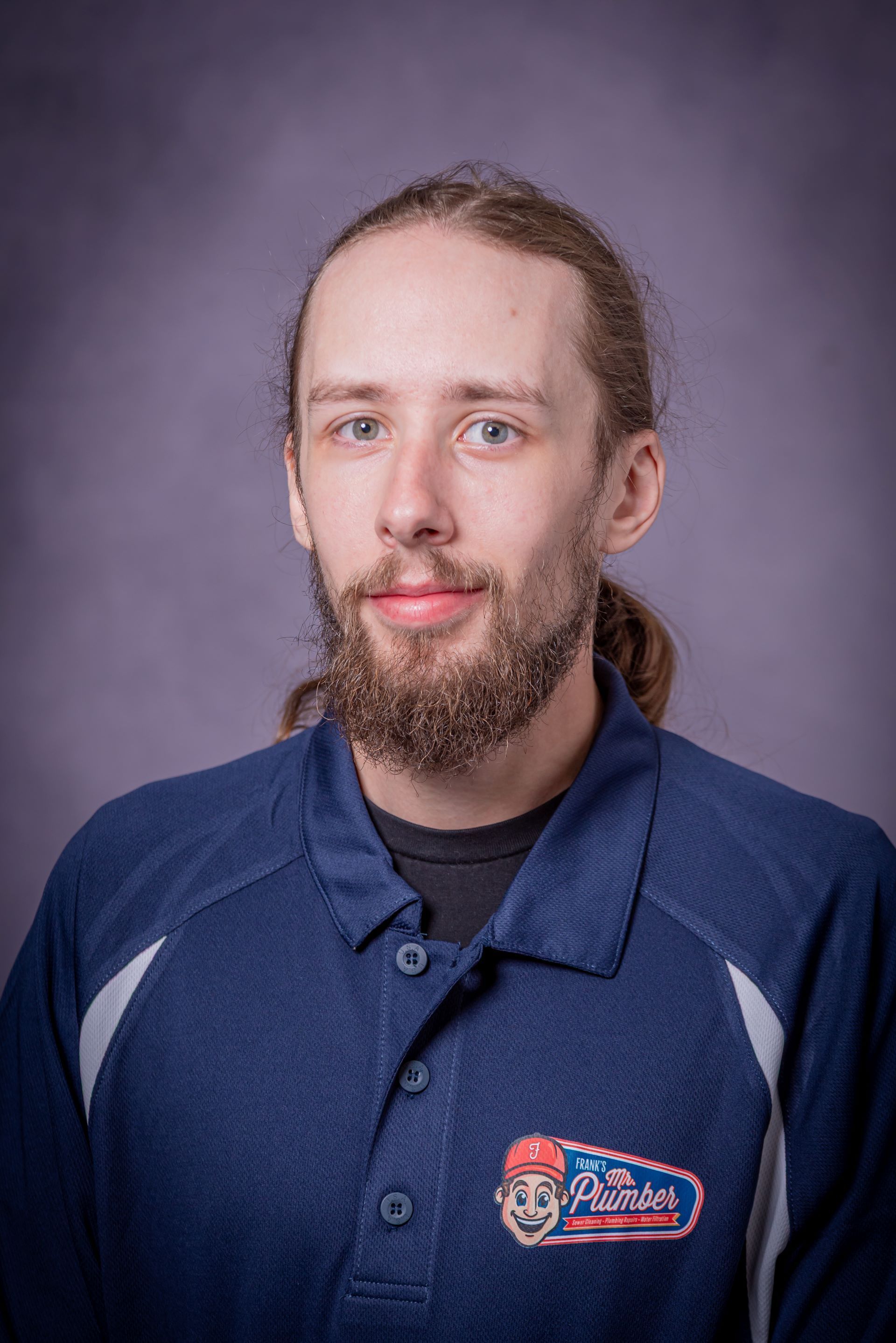 A man with a beard and long hair is wearing a blue polo shirt.