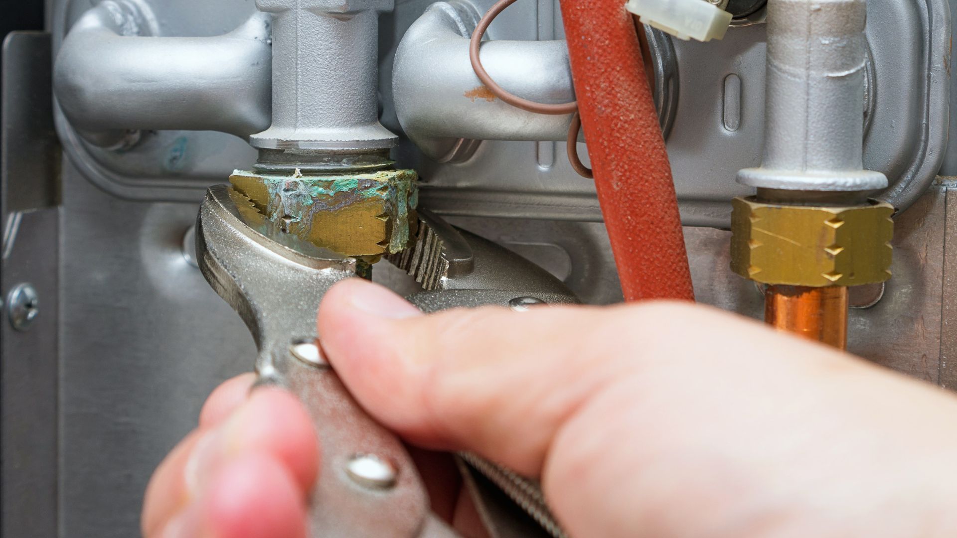 A person's hand using pliers to tighten a nut on a water heater component.
