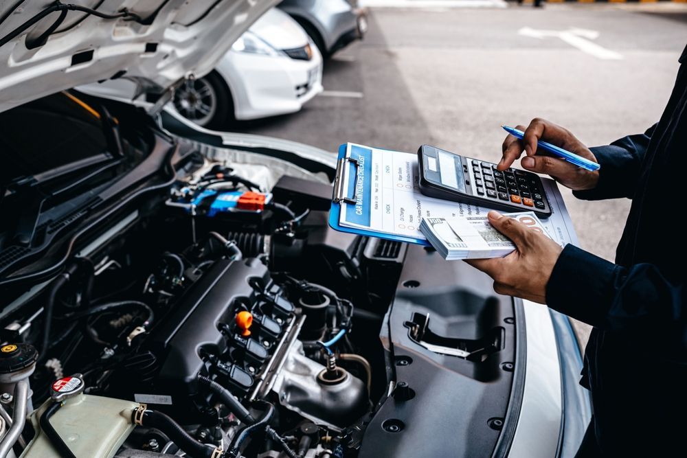 A Man is Working on the Engine of a Car While Holding a Clipboard — Auto Blue Service Centre In Bungalow, QLD