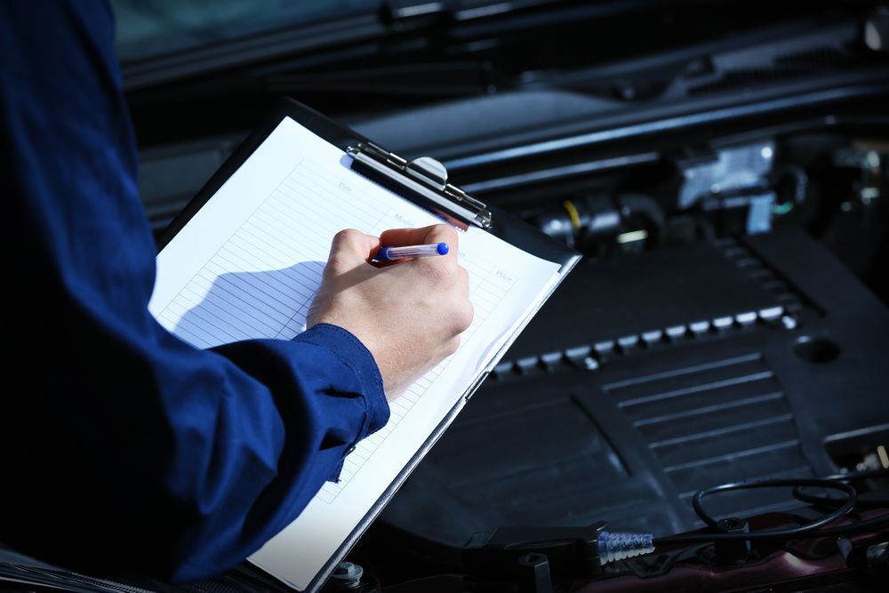 A Person is Writing on a Clipboard in Front of a Car Engine — Auto Blue Service Centre In Bungalow, QLD