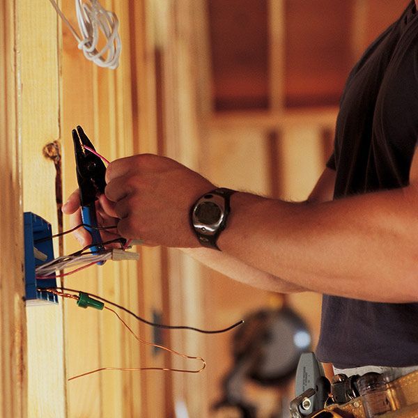 Electrician wiring a wall, connecting blue and green wires in a wooden room.