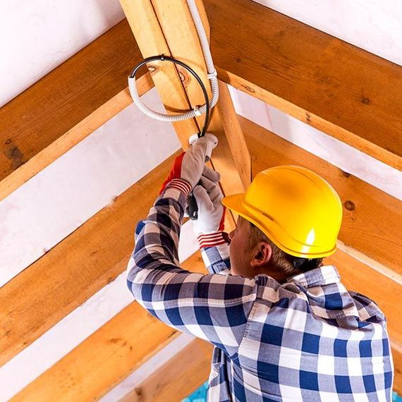 Construction worker in yellow hard hat fastening a wooden beam in a ceiling corner