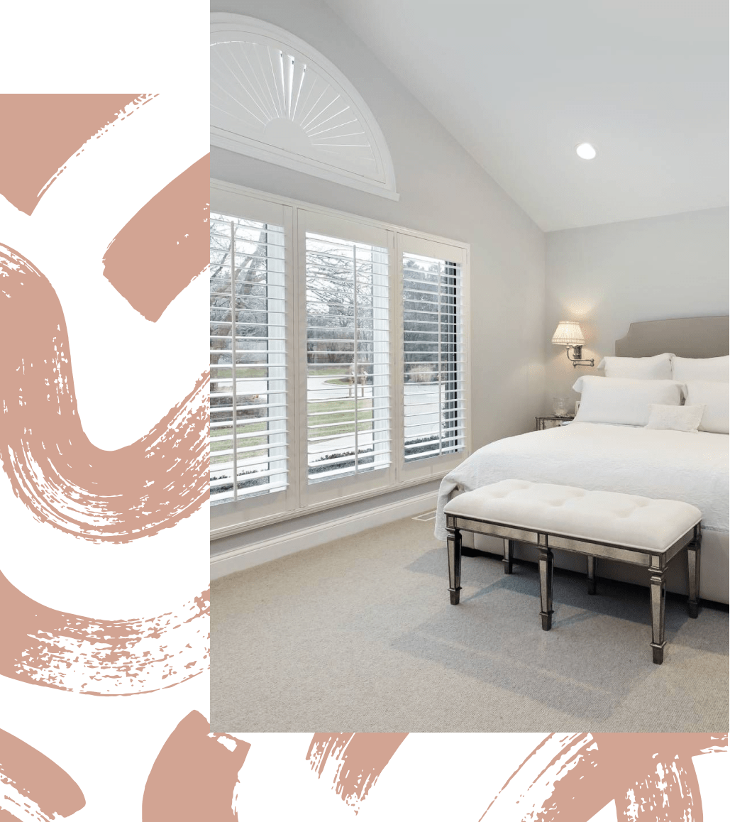 White plantation shutters over a bedroom window with bed and ottoman in the foreground
