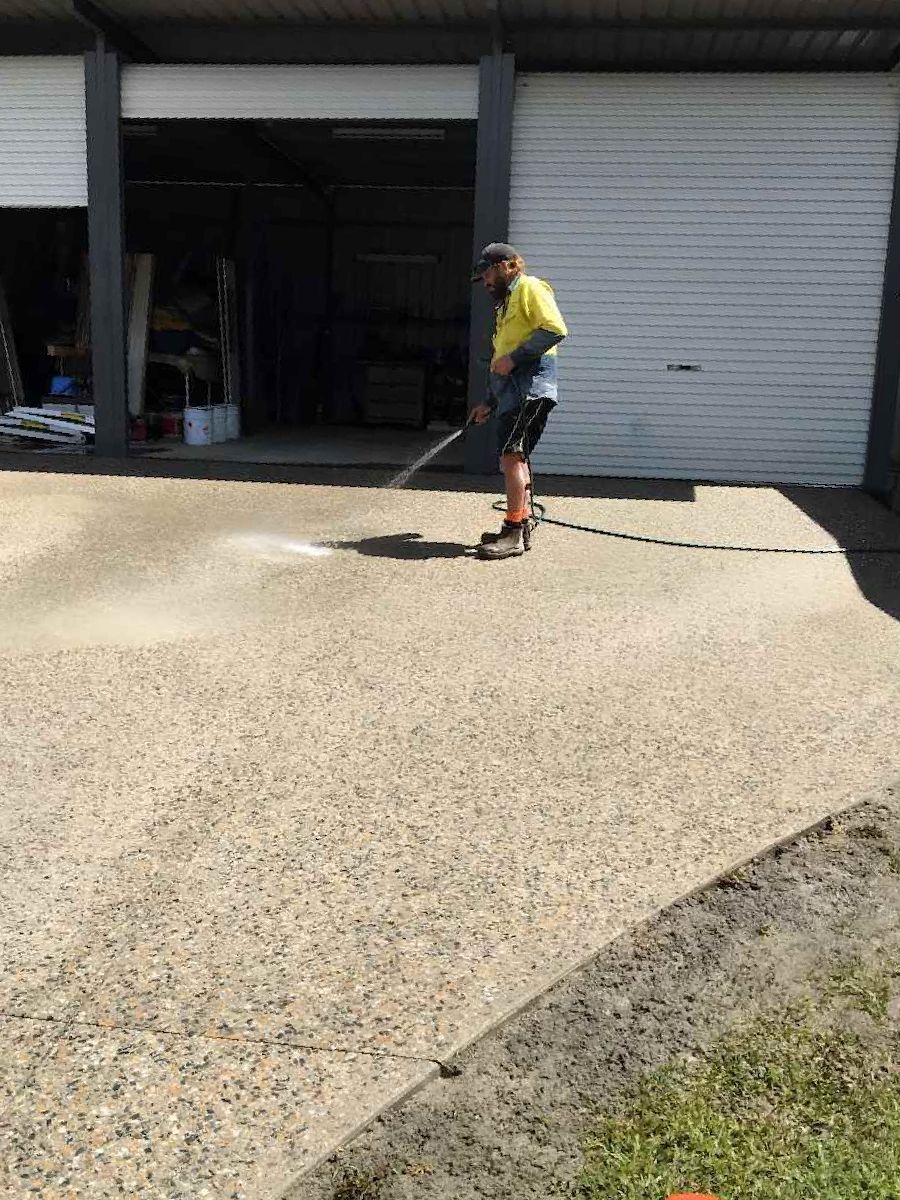 A Man Is Cleaning A Driveway With A Broom — Tropical North Concreting In Trinity Park, QLD
