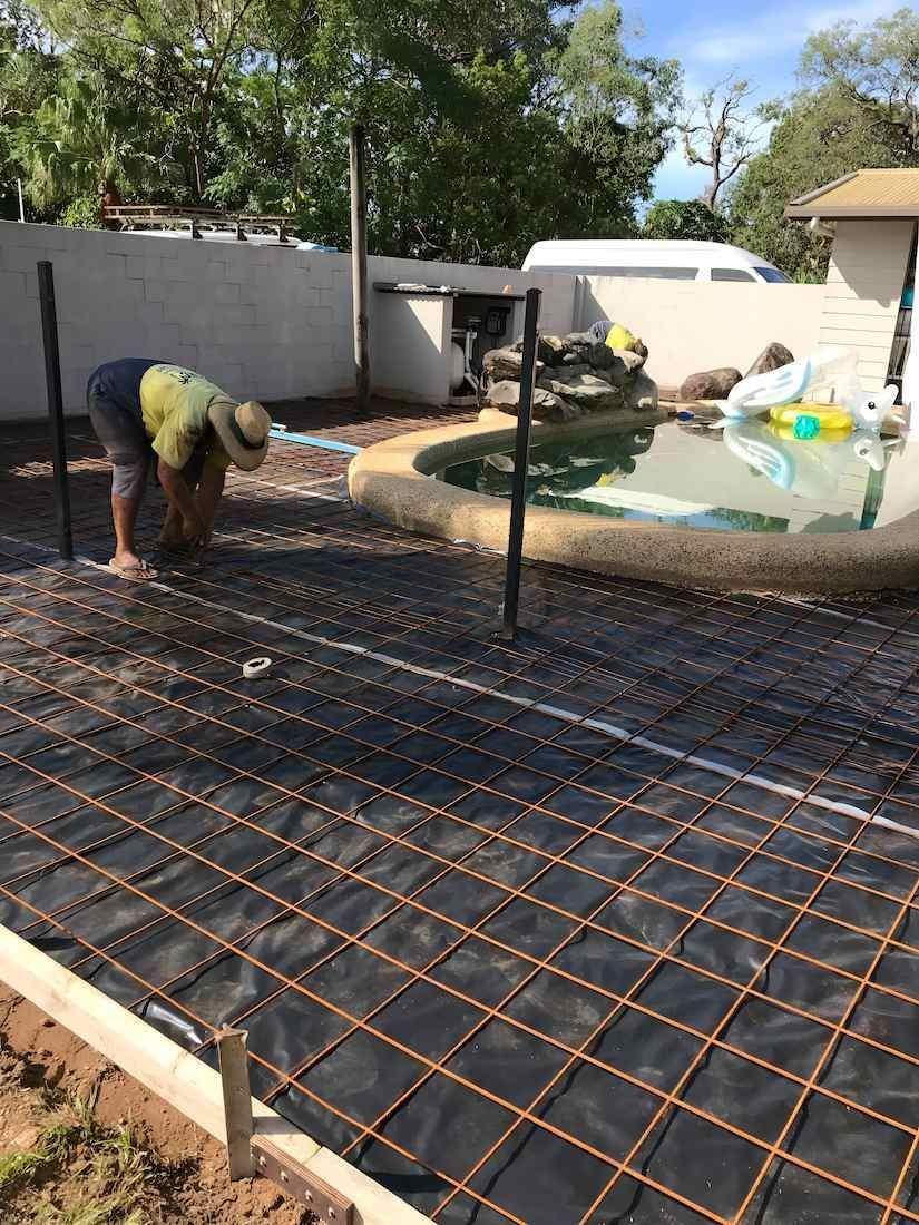 A Man Is Working On A Concrete Patio Next To A Pool — Tropical North Concreting In Trinity Park, QLD