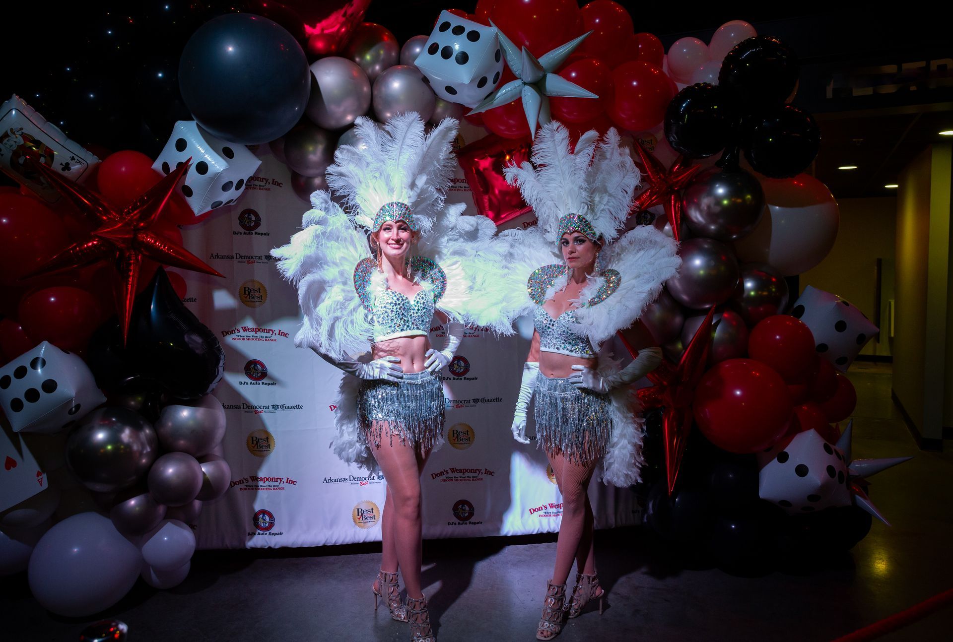 Two women in carnival costumes are standing in front of a wall of balloons.