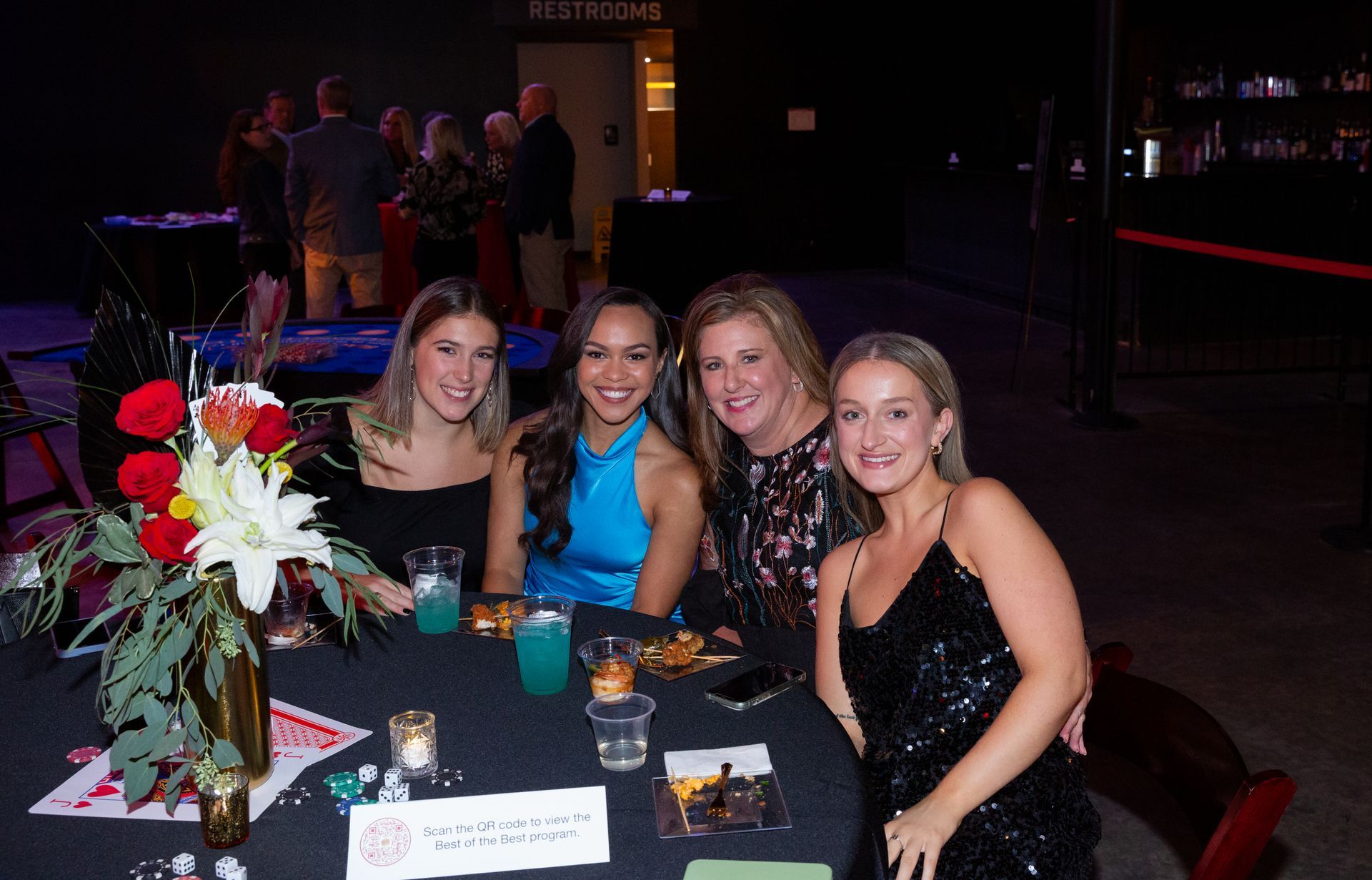 A group of women are sitting at a table with drinks and flowers.