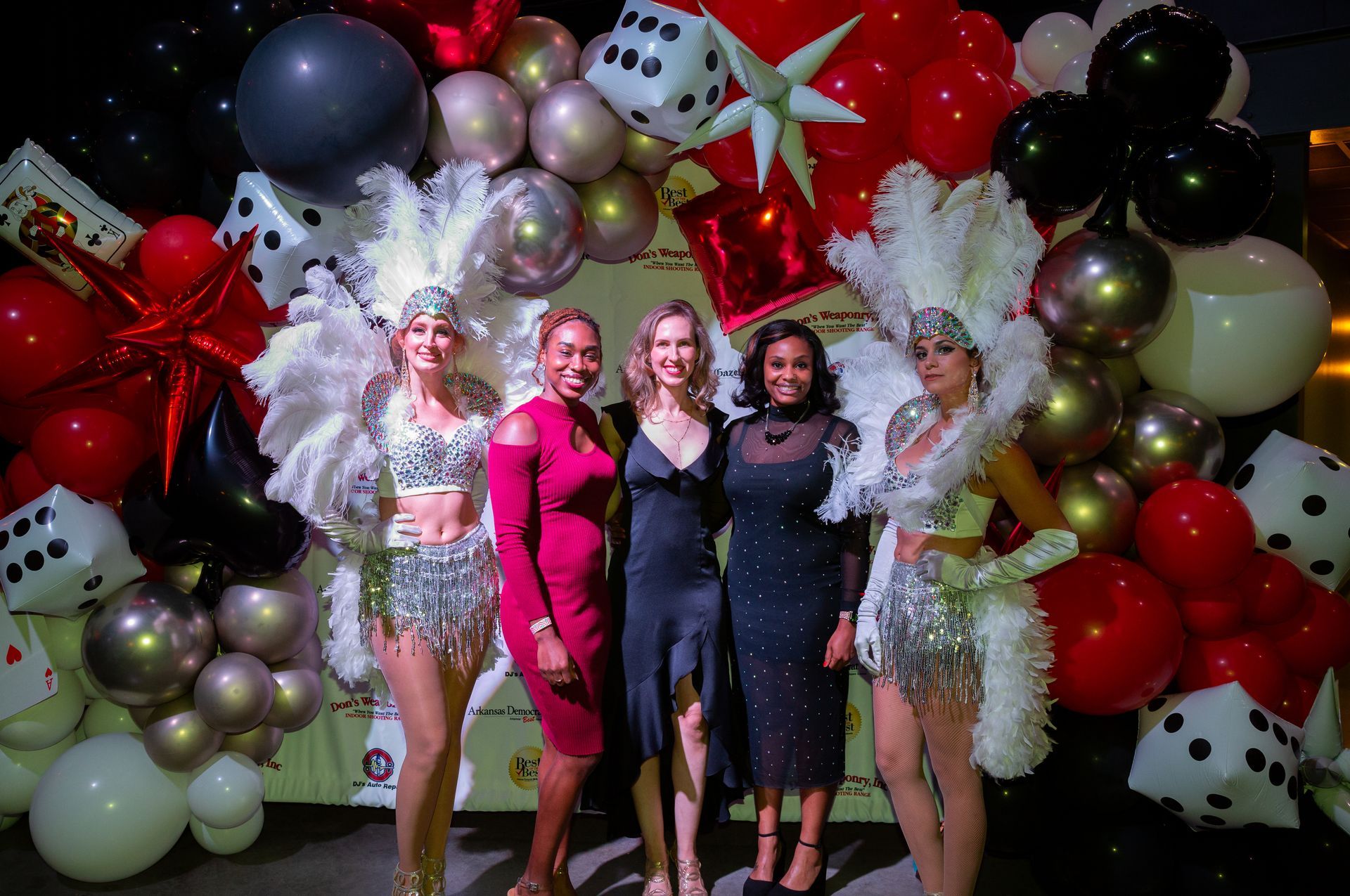 A group of women are posing for a picture in front of a wall of balloons.