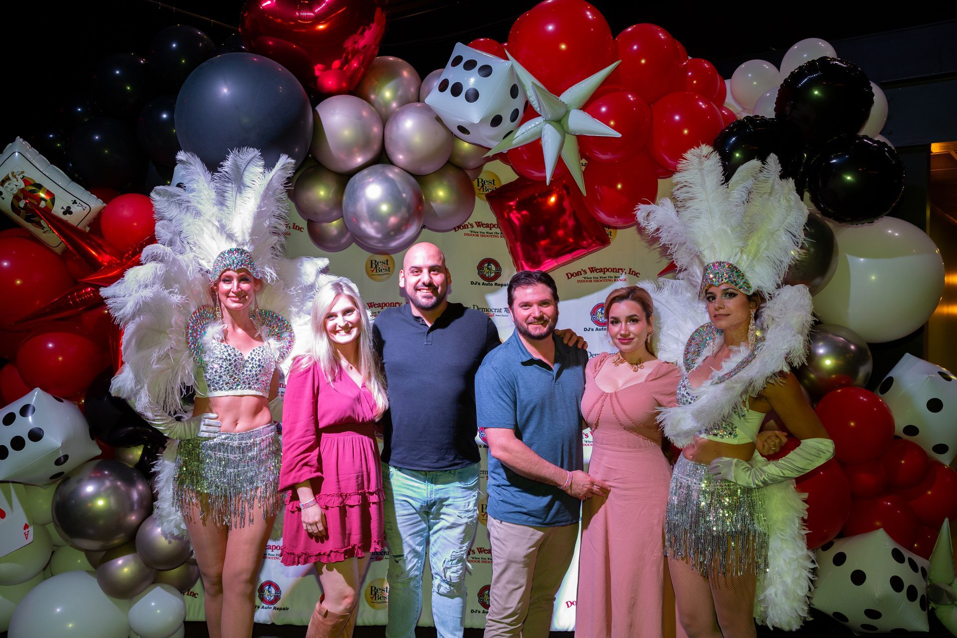 A group of people are posing for a picture in front of a wall of balloons.