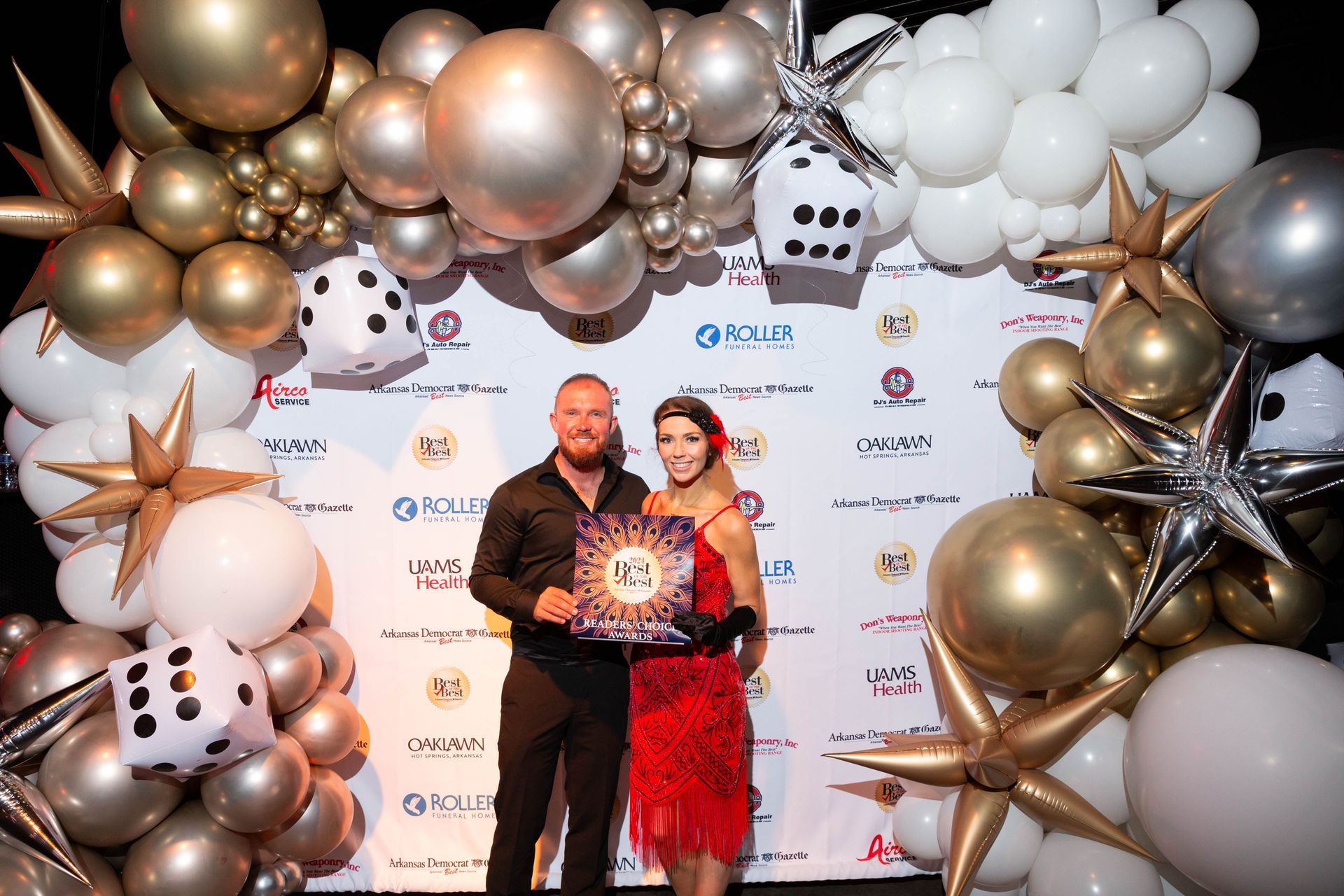 A man and a woman are standing in front of a wall of balloons.