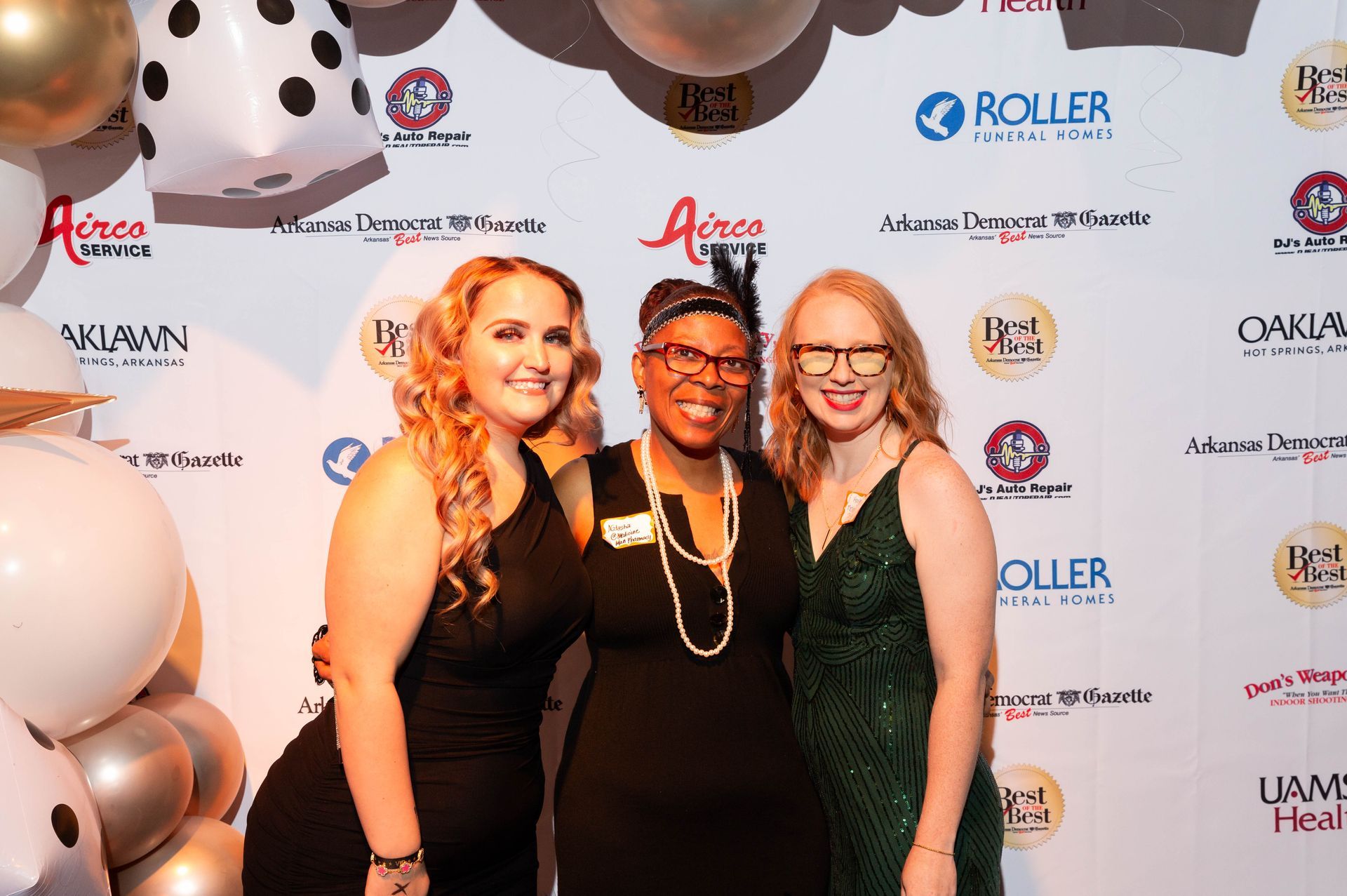 Three women are posing for a picture in front of a wall with balloons.