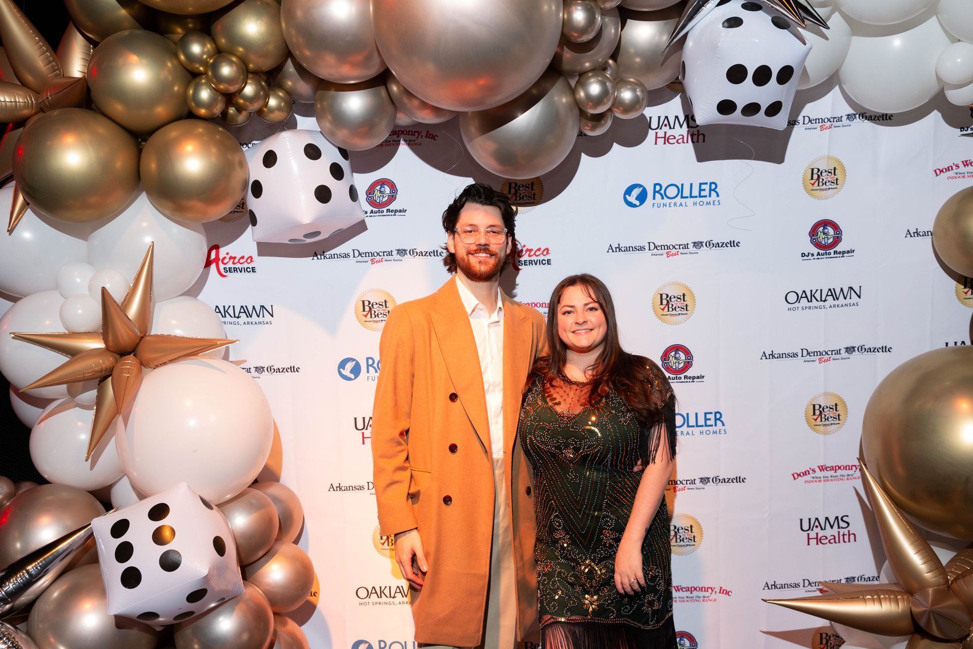 A man and a woman are standing in front of a wall of balloons and dice.