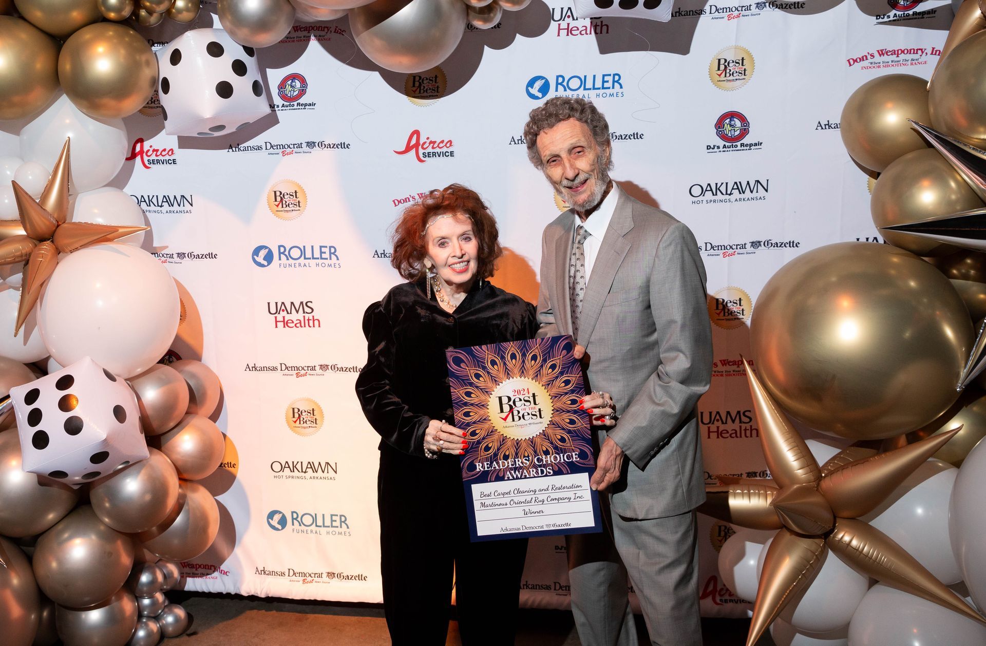 A man and a woman are standing in front of a wall of balloons.