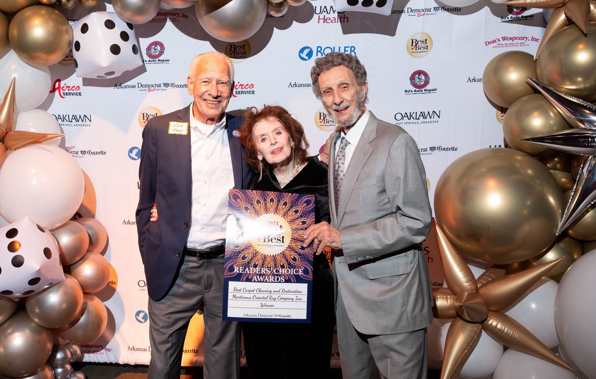 Three men and a woman are posing for a picture in front of balloons.