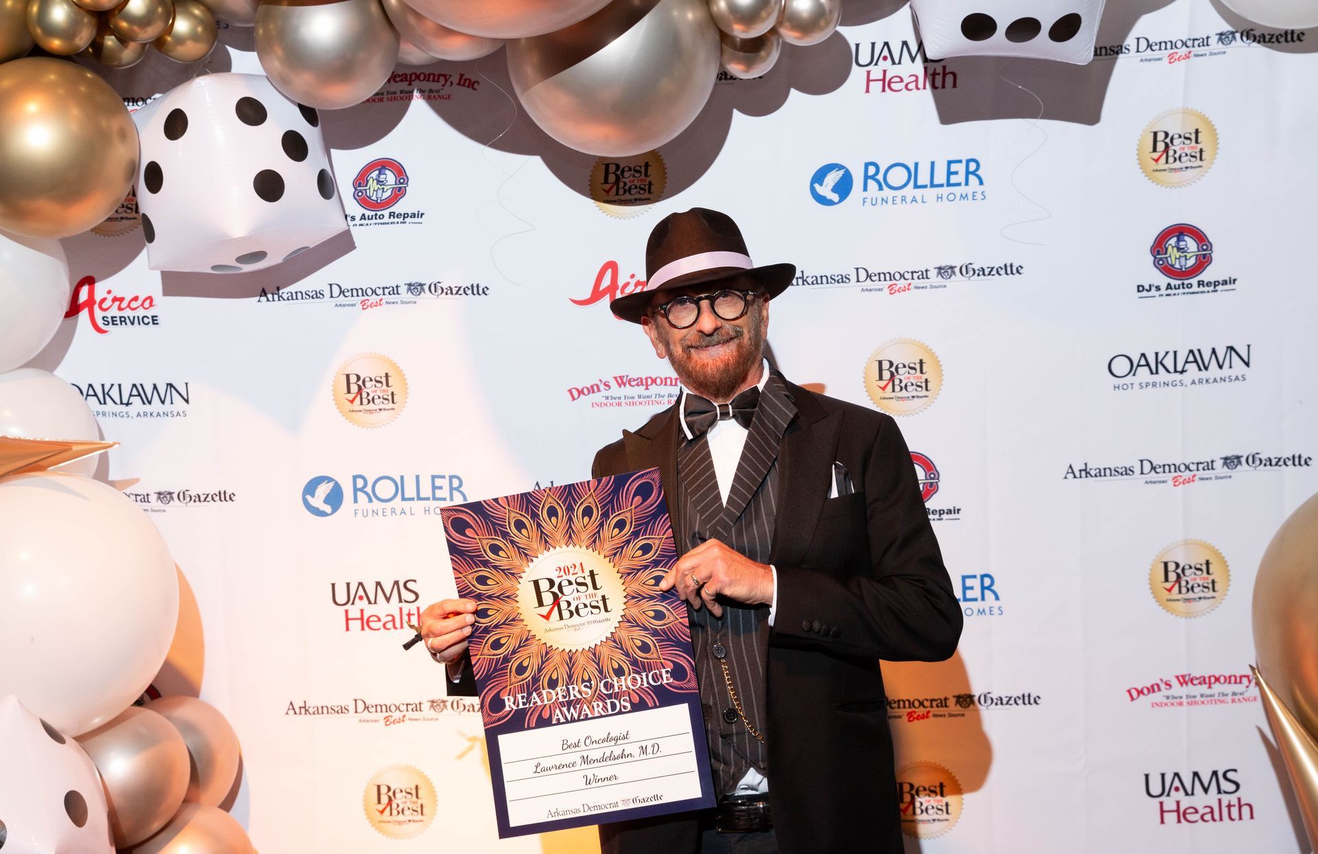 A man in a suit and hat is holding a sign in front of balloons.