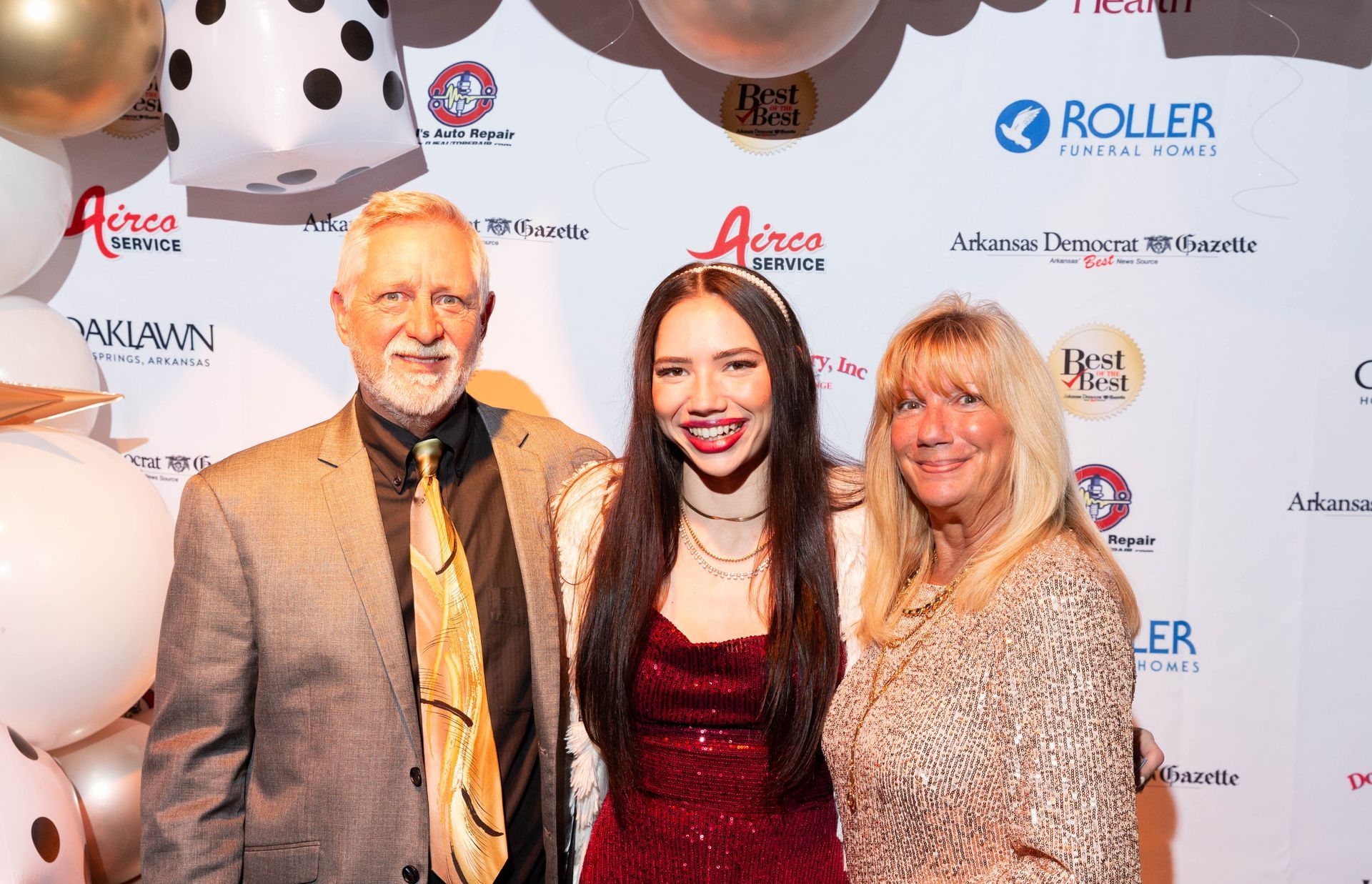 A man and two women are posing for a picture on a red carpet.
