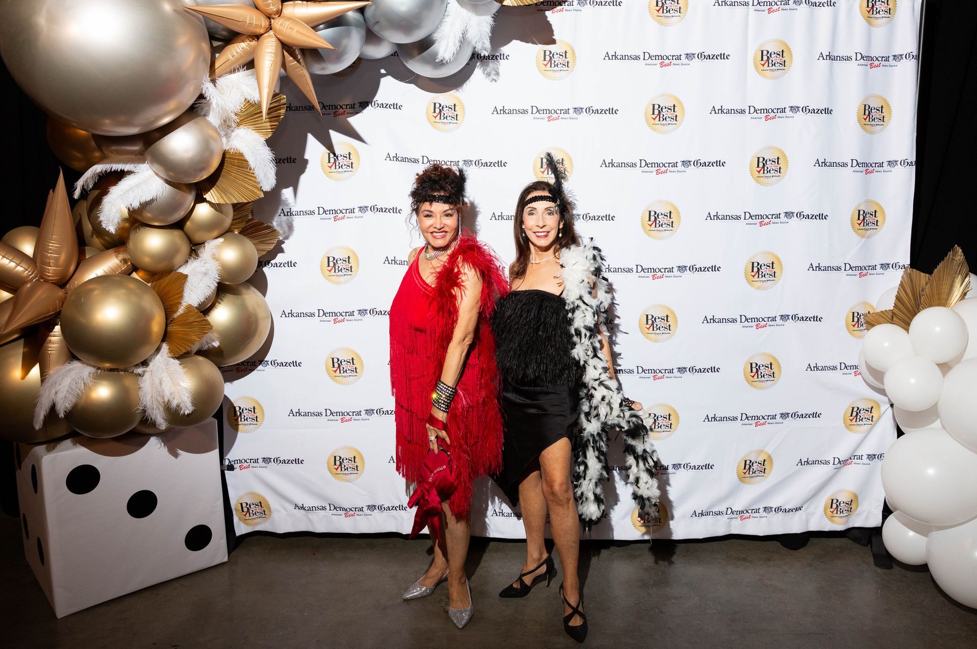 Two women are standing next to each other in front of a wall covered in balloons.