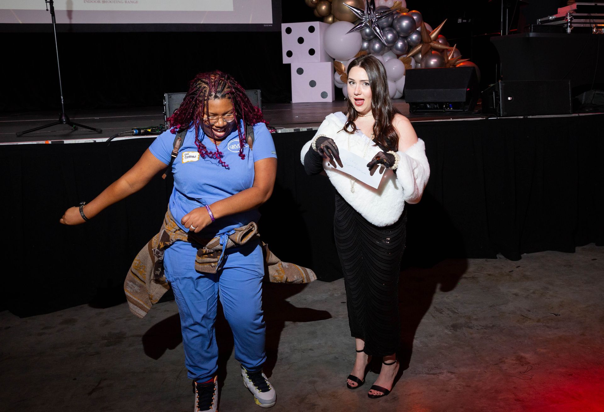 Two women are dancing on a stage with balloons in the background.