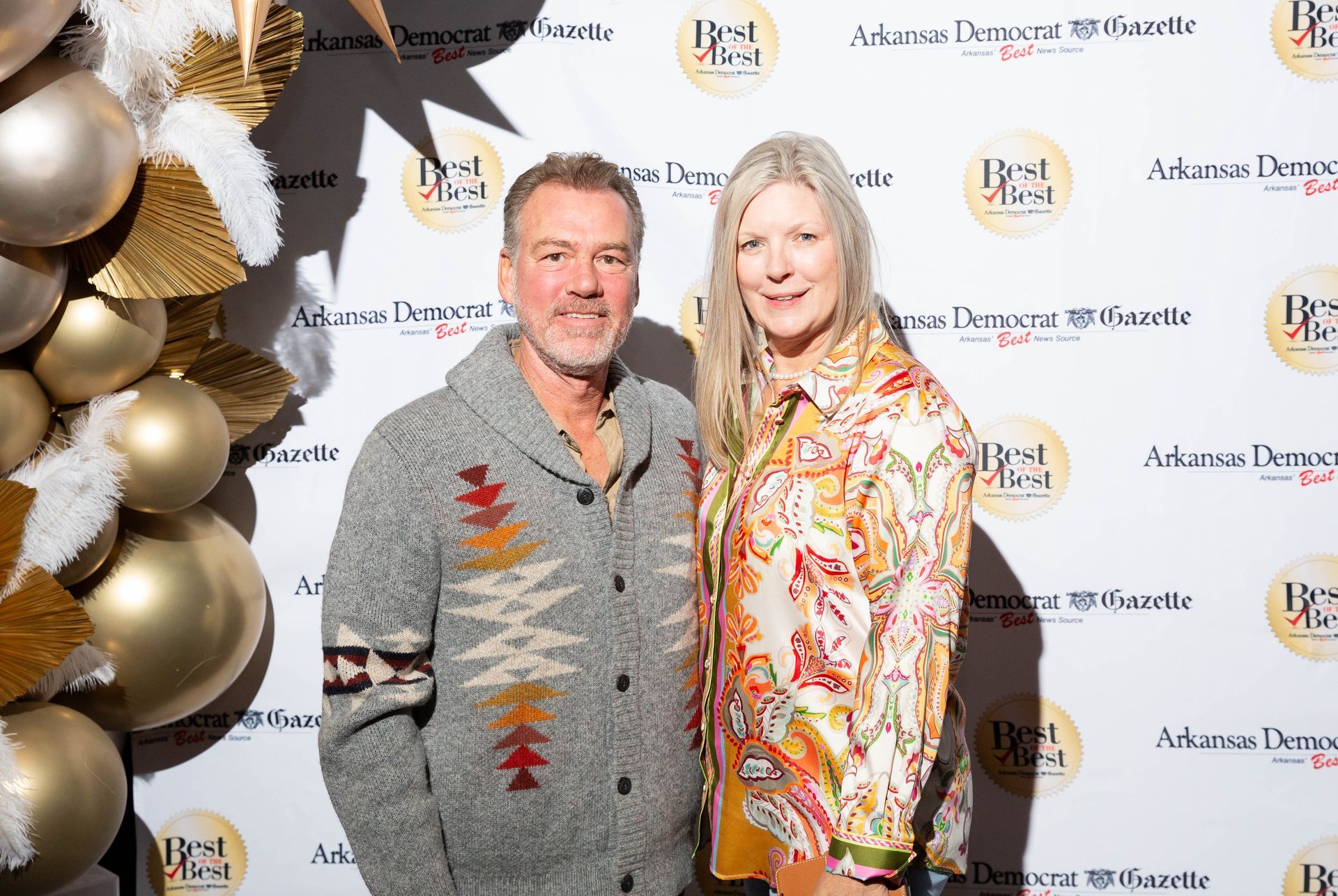 A man and a woman are posing for a picture in front of a wall with balloons.