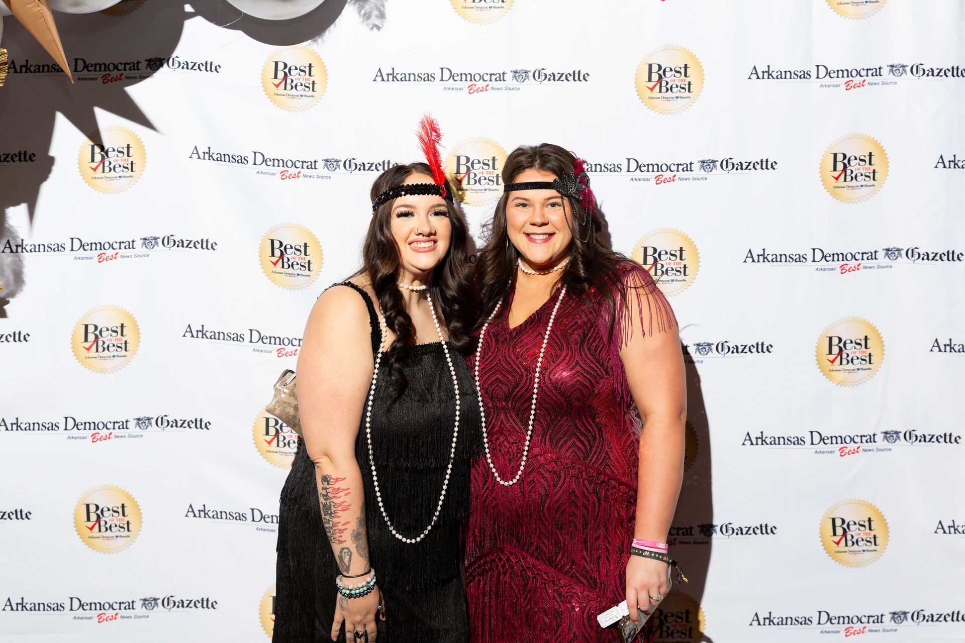 Two women are posing for a picture in front of a wall.
