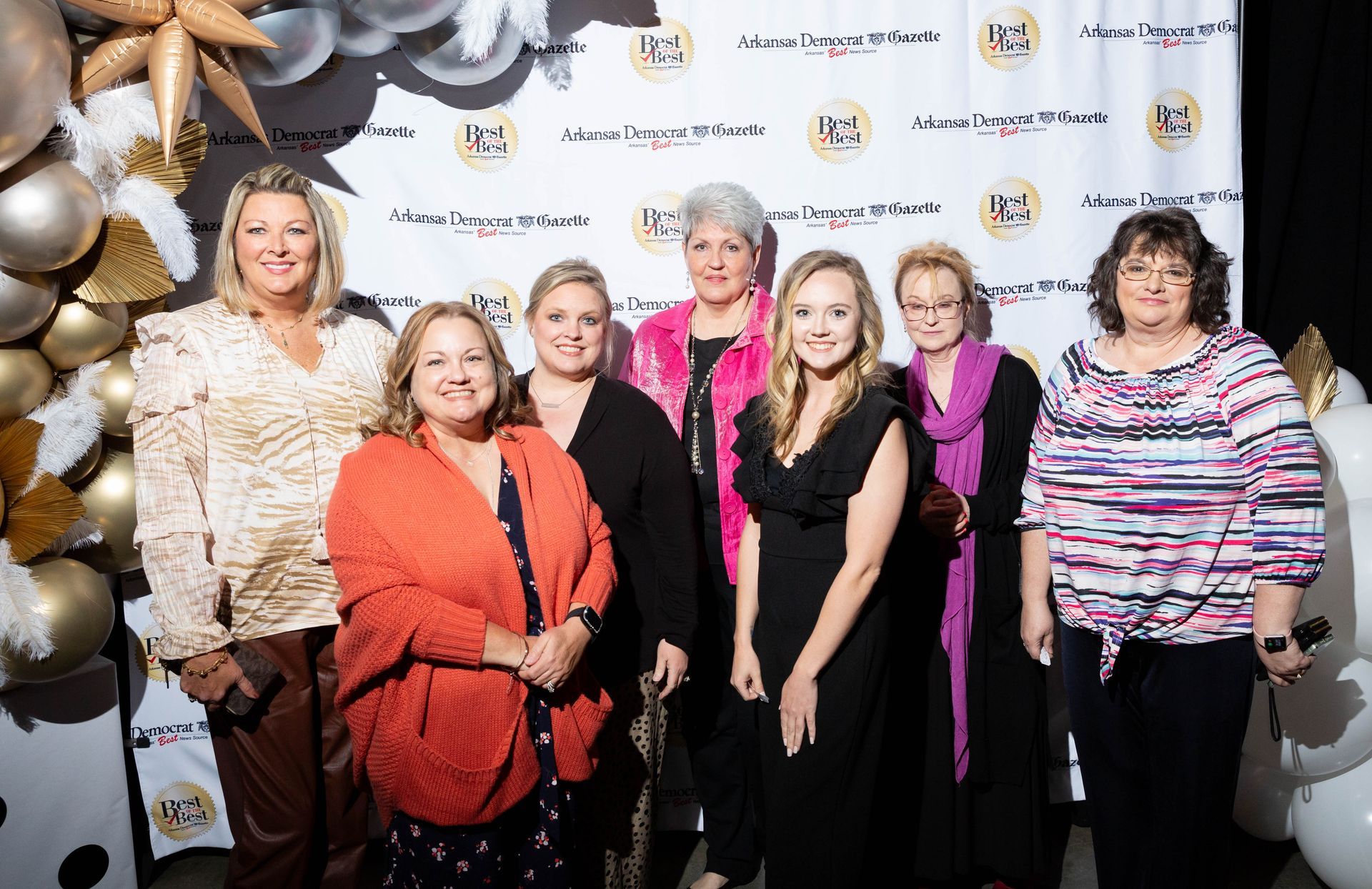 A group of women are posing for a picture in front of balloons.