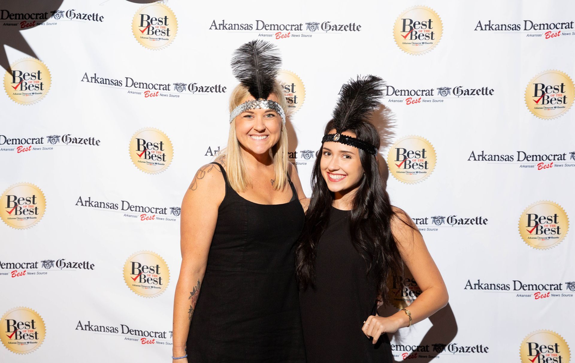 Two women are posing for a picture in front of a white backdrop.