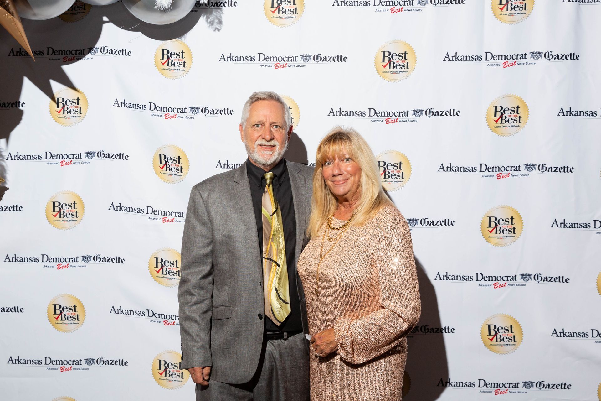 A man and a woman are posing for a picture in front of a backdrop.