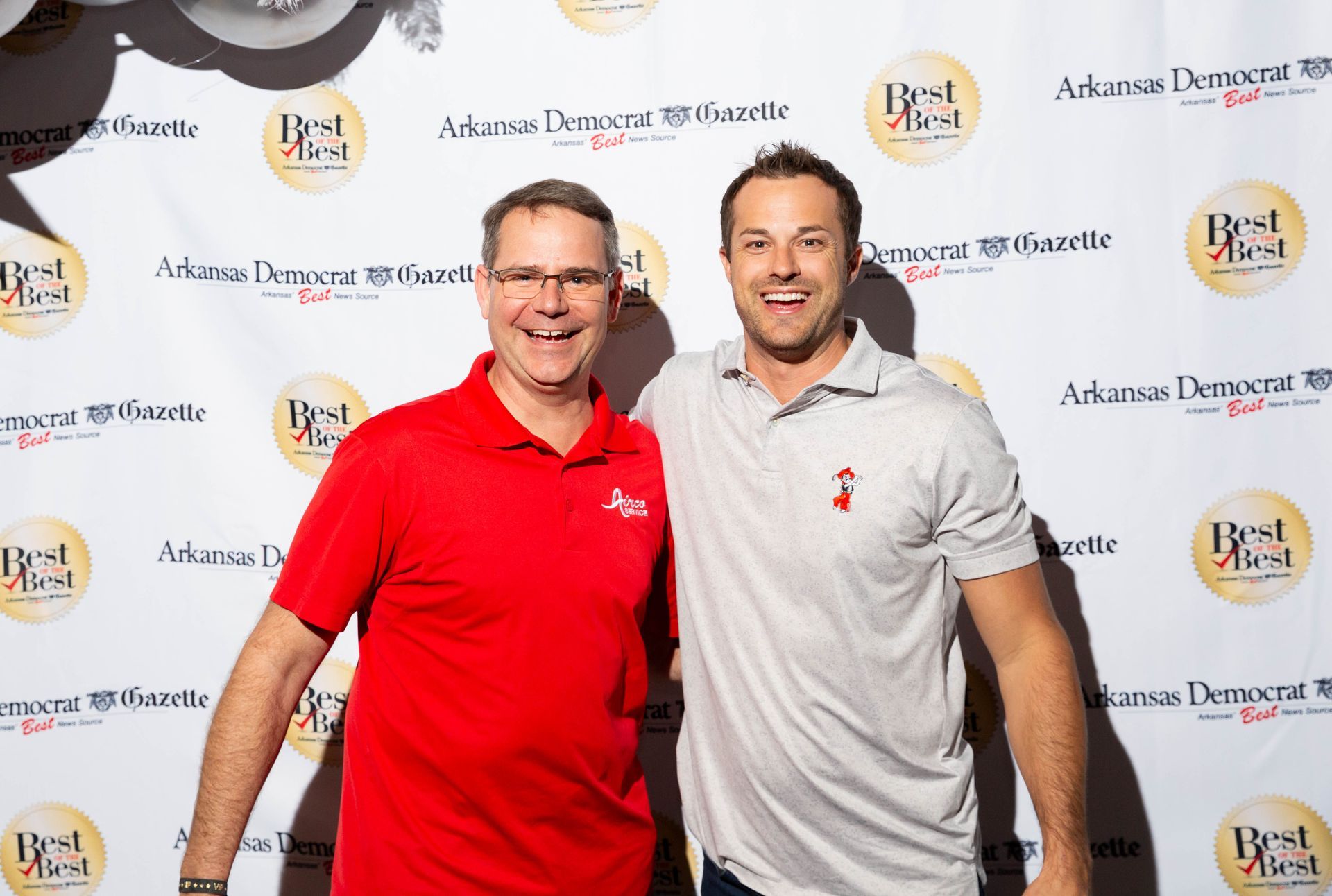 Two men are posing for a picture in front of a backdrop that says best meal.