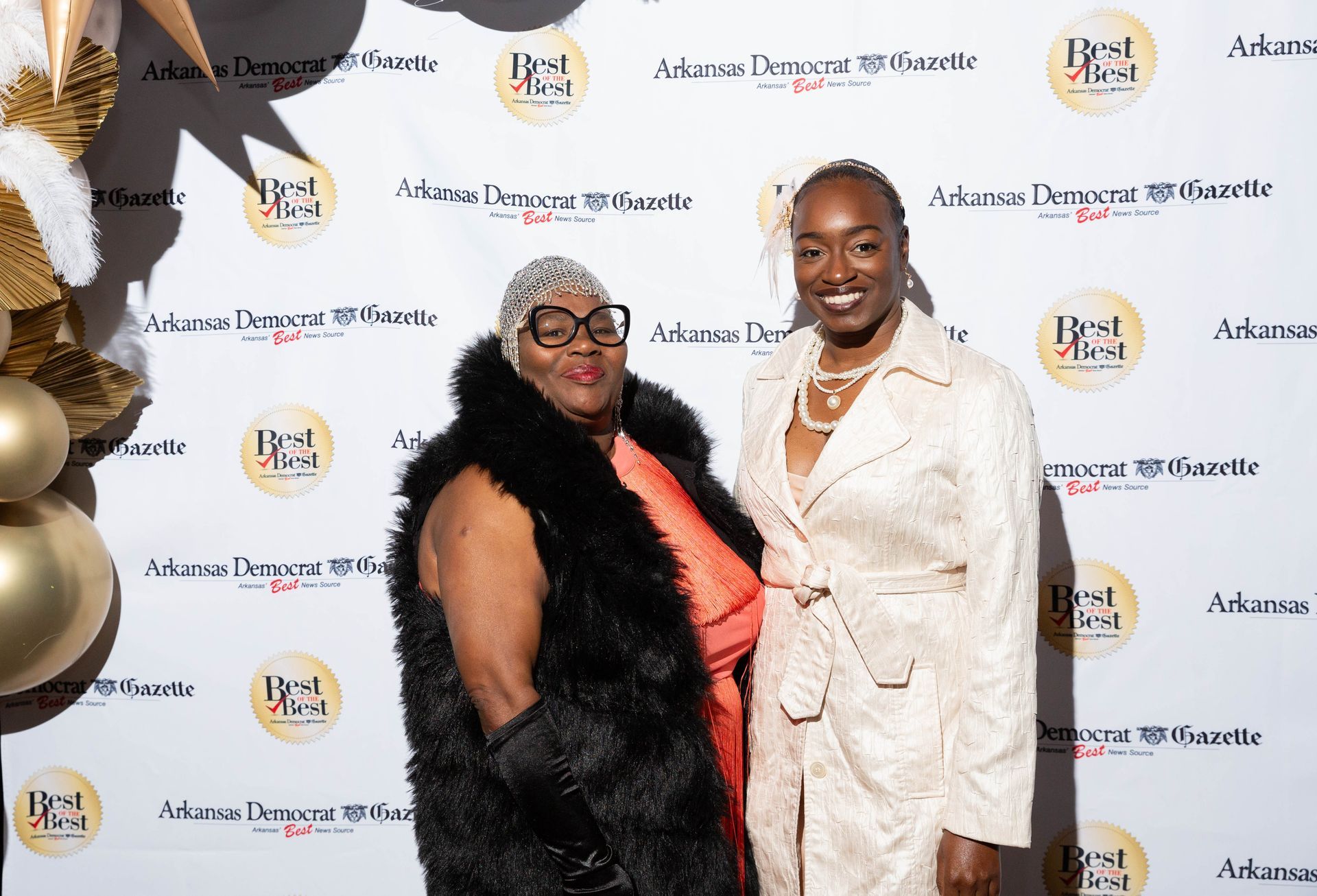 Two women are standing next to each other in front of a wall.