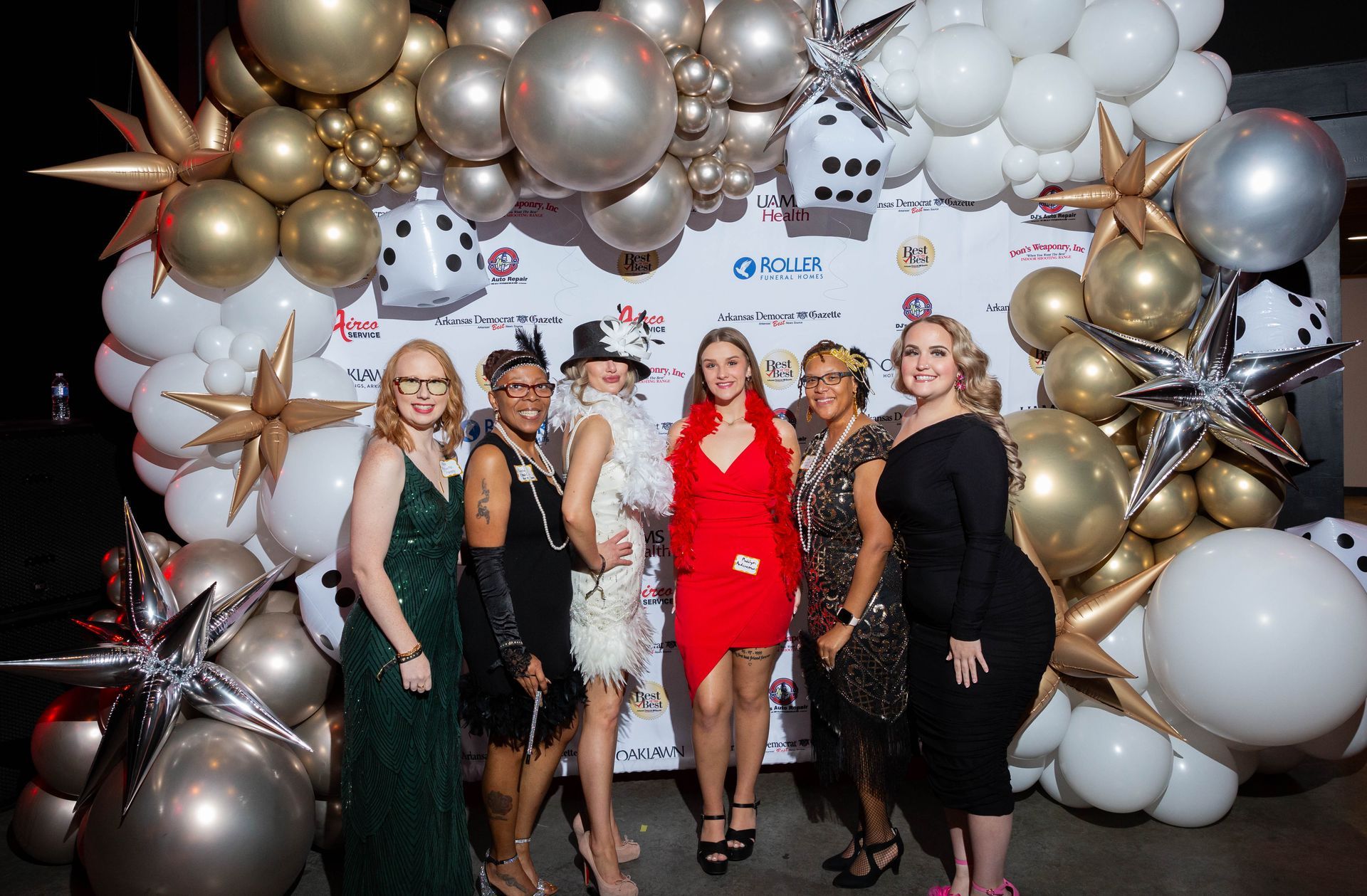 A group of women are posing for a picture in front of a wall of balloons.
