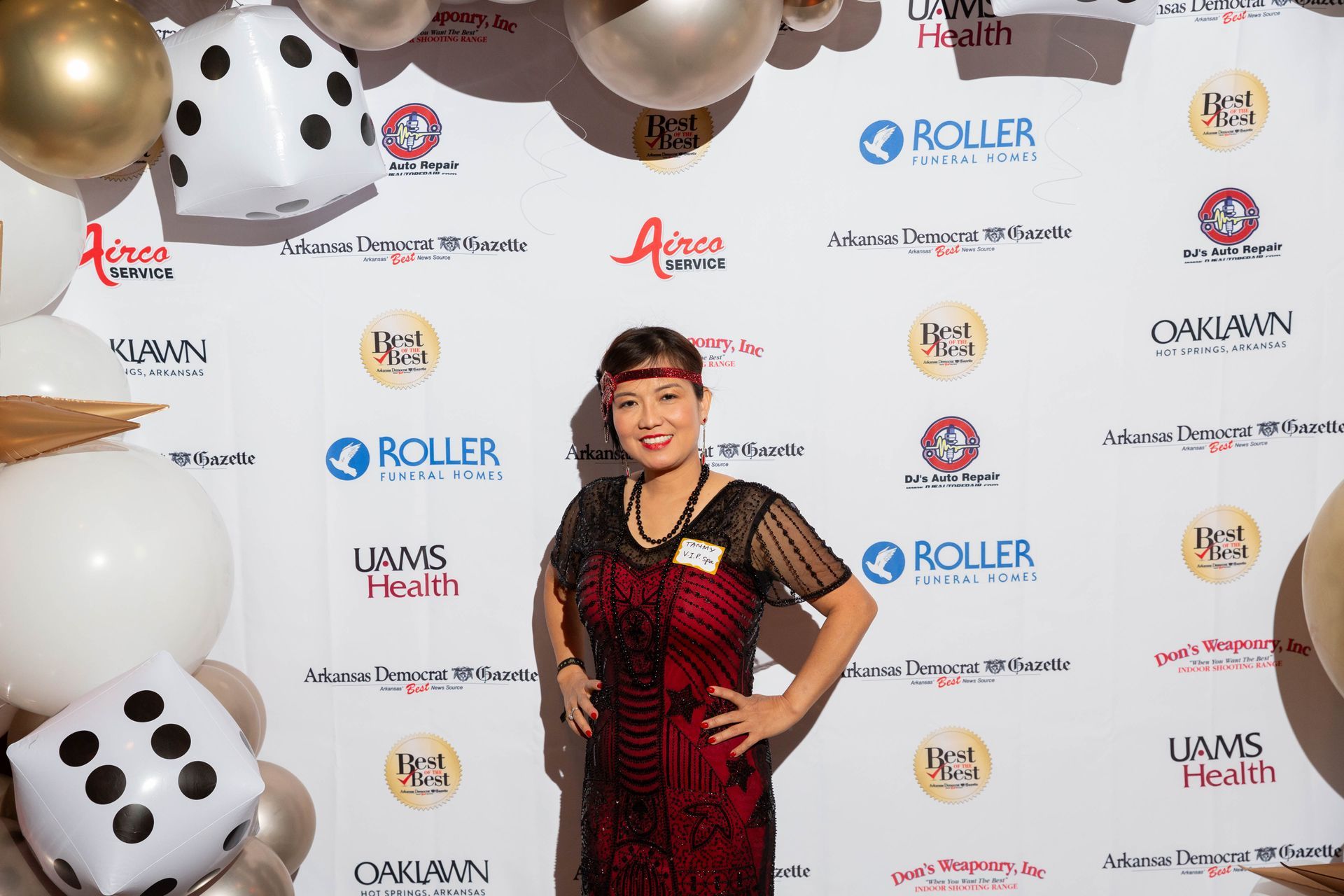 A woman in a red dress is standing in front of a wall of balloons.