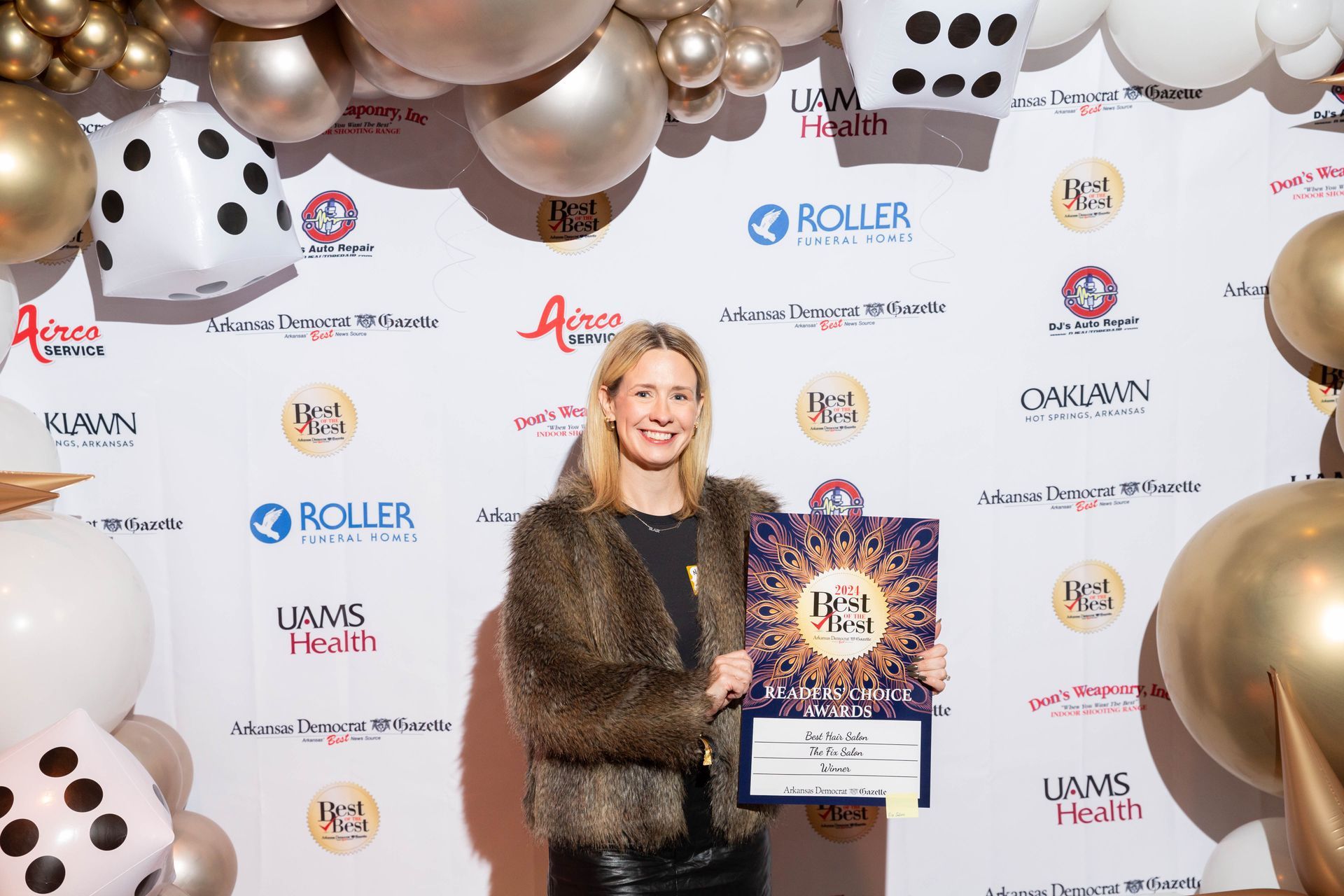 A woman is standing in front of a wall of balloons holding a certificate.