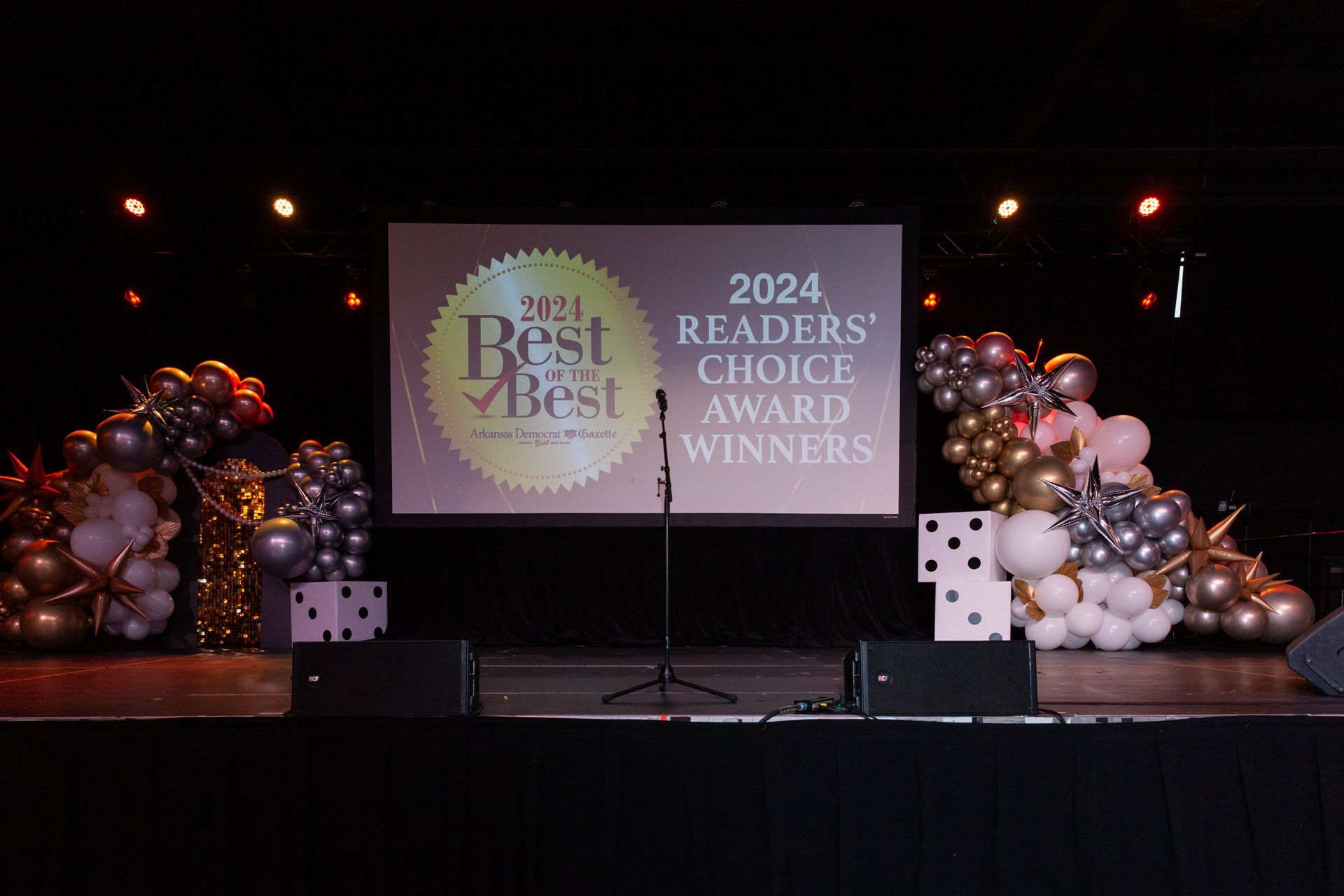 A stage with balloons and a projector screen for the readers choice award winners.