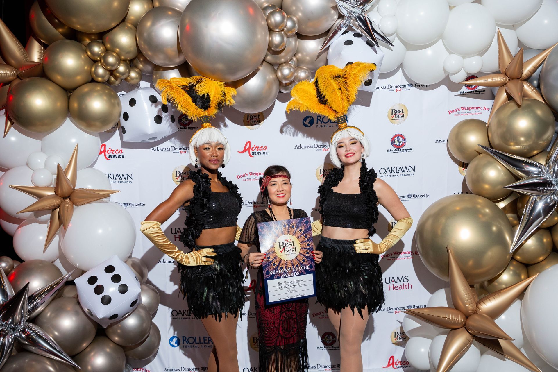 Three women are standing in front of a wall of balloons.